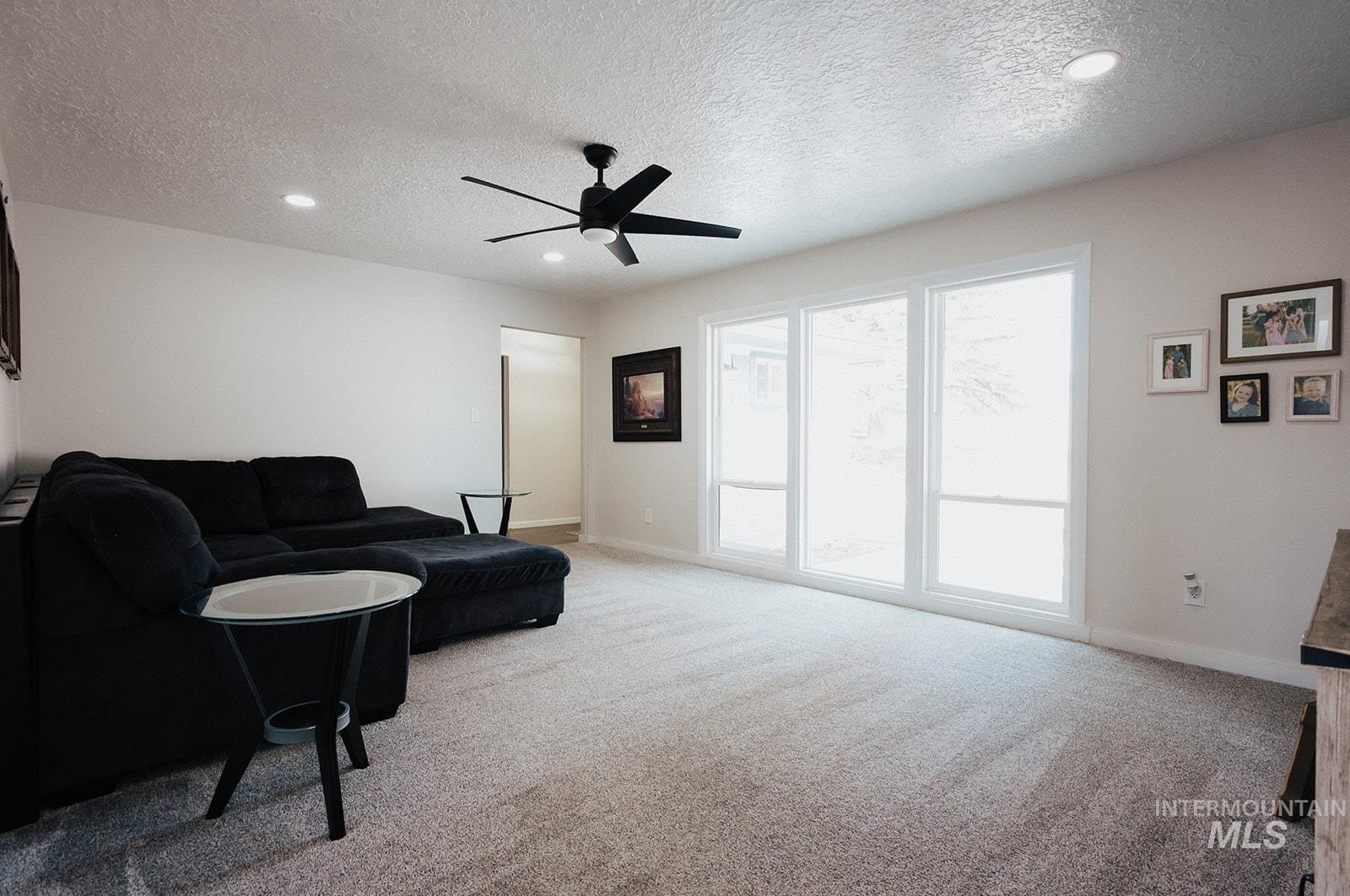 Living room featuring a textured ceiling, light colored carpet, recessed lighting, and ceiling fan