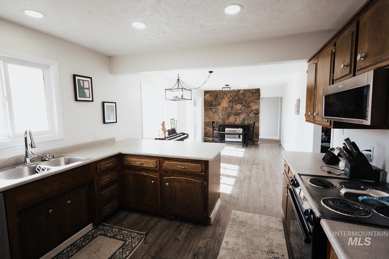 Kitchen featuring dark brown cabinets, a peninsula, black electric range oven, light countertops, and dark wood-style floors