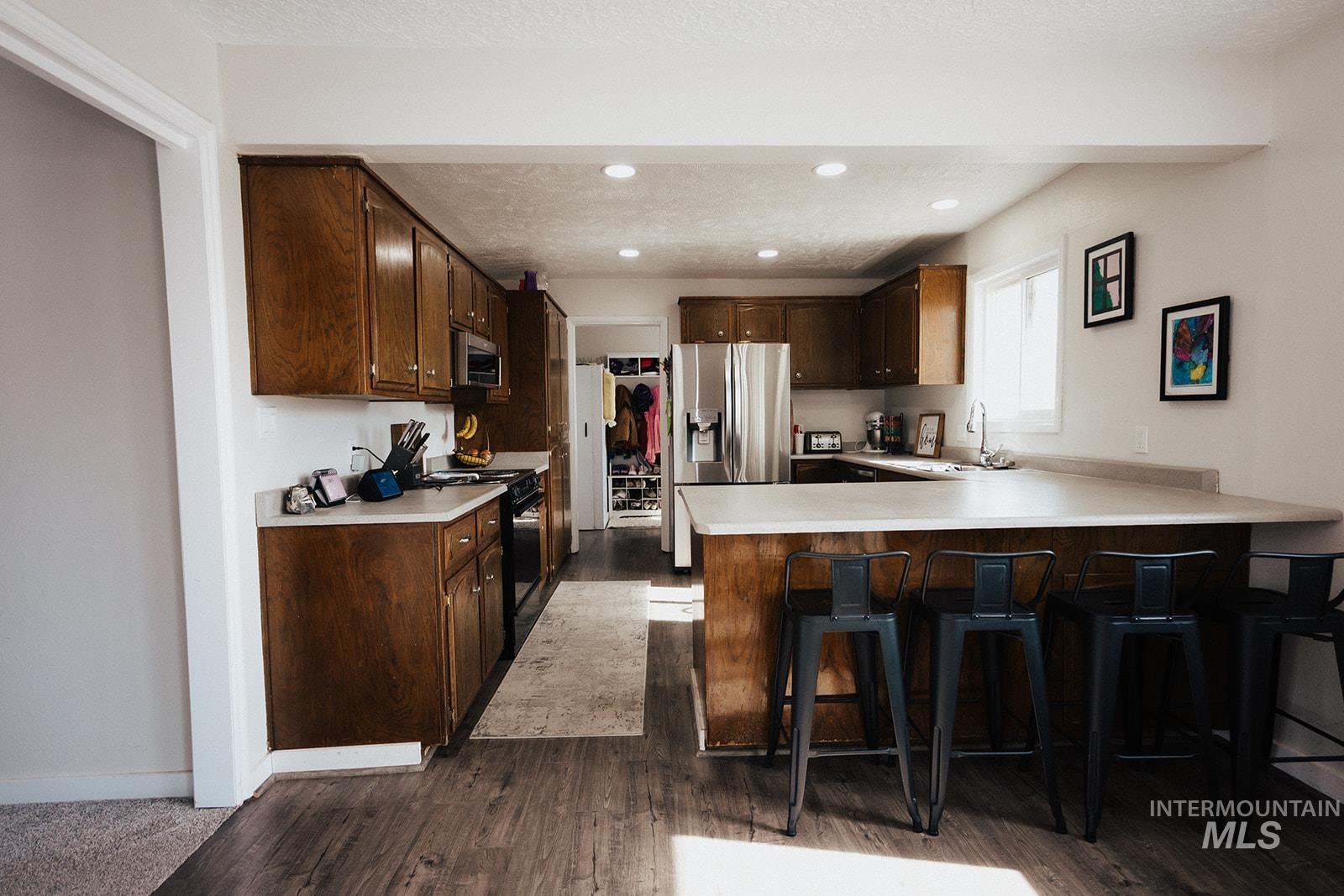 Kitchen with light countertops, dark brown cabinets, appliances with stainless steel finishes, a kitchen breakfast bar, and a peninsula