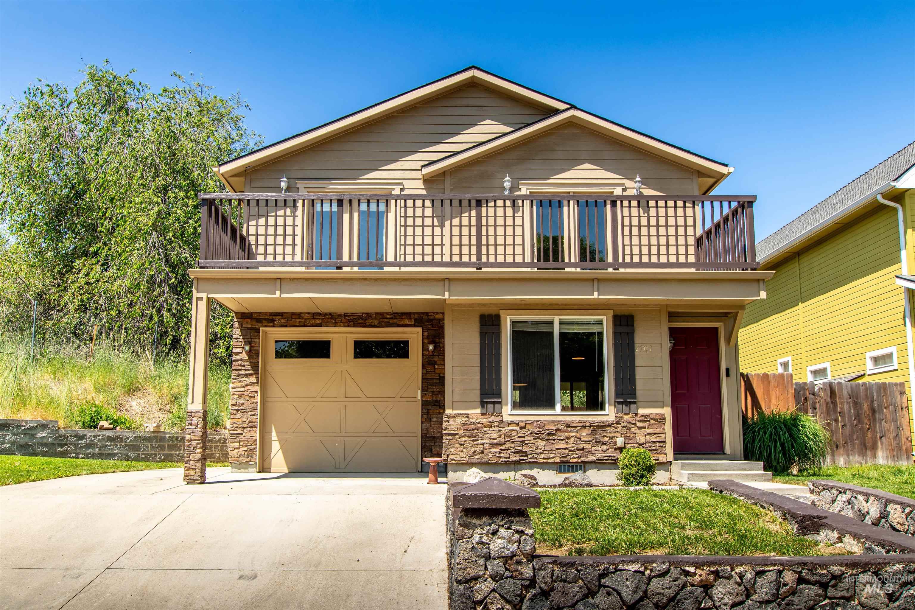 View of front of home with concrete driveway, a balcony, a garage, and stone siding
