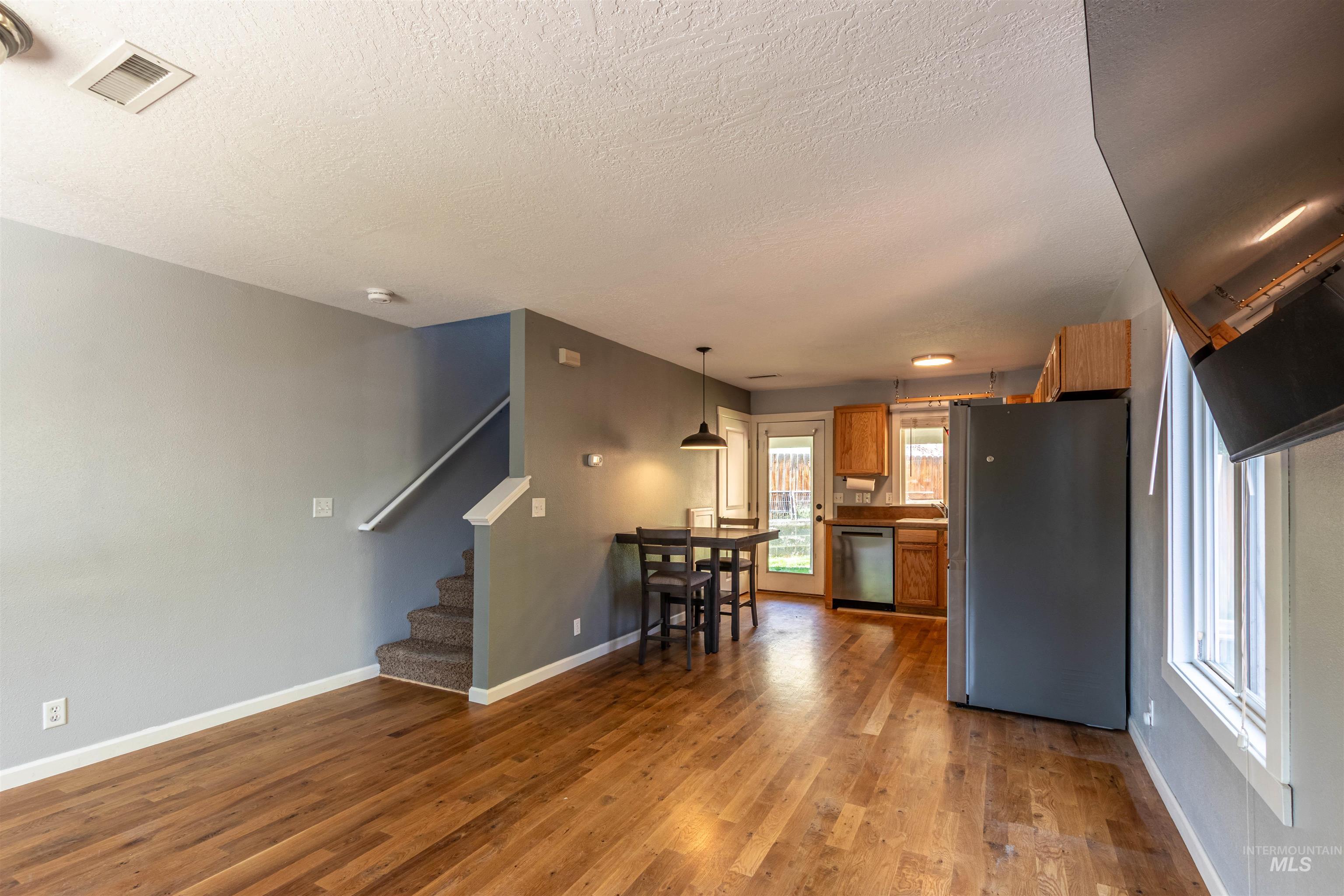 Kitchen featuring brown cabinetry, appliances with stainless steel finishes, pendant lighting, light wood finished floors, and a textured ceiling