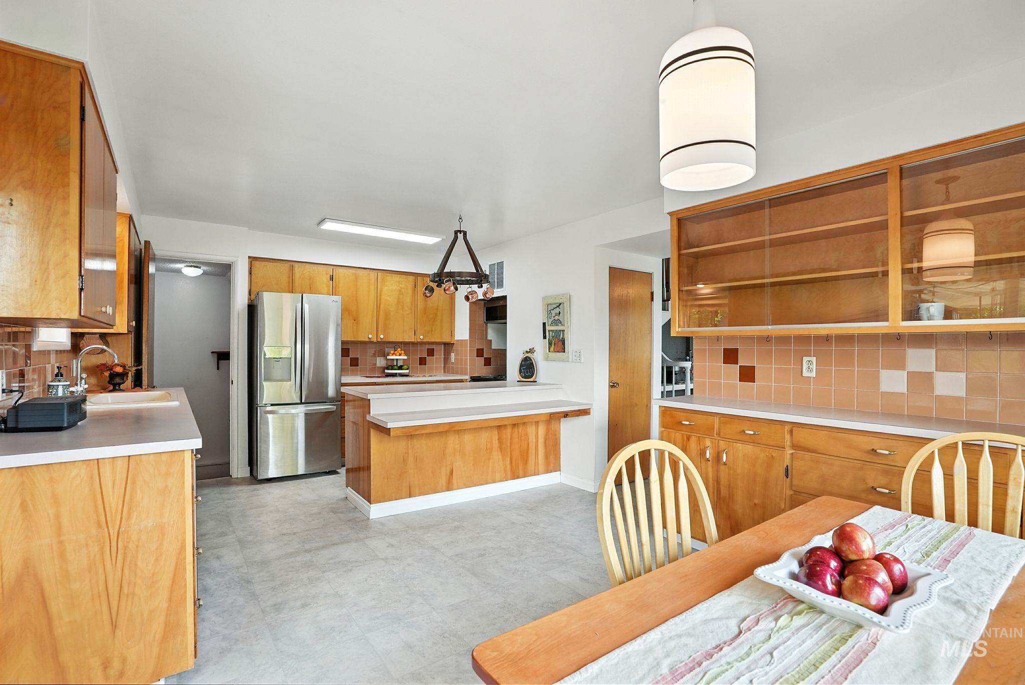 Kitchen with backsplash, light countertops, brown cabinetry, and stainless steel fridge