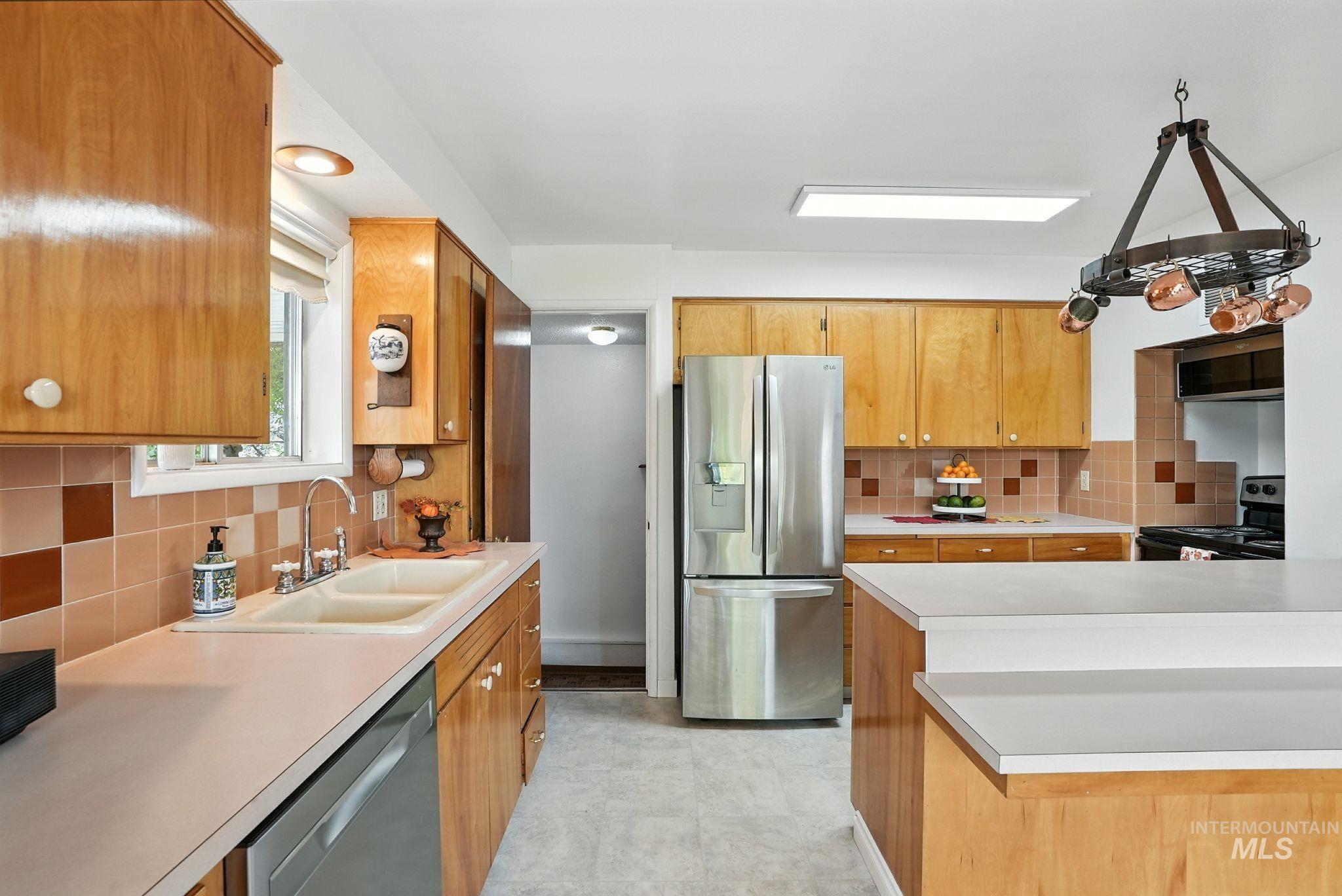 Kitchen featuring backsplash, stainless steel appliances, light countertops, and brown cabinetry