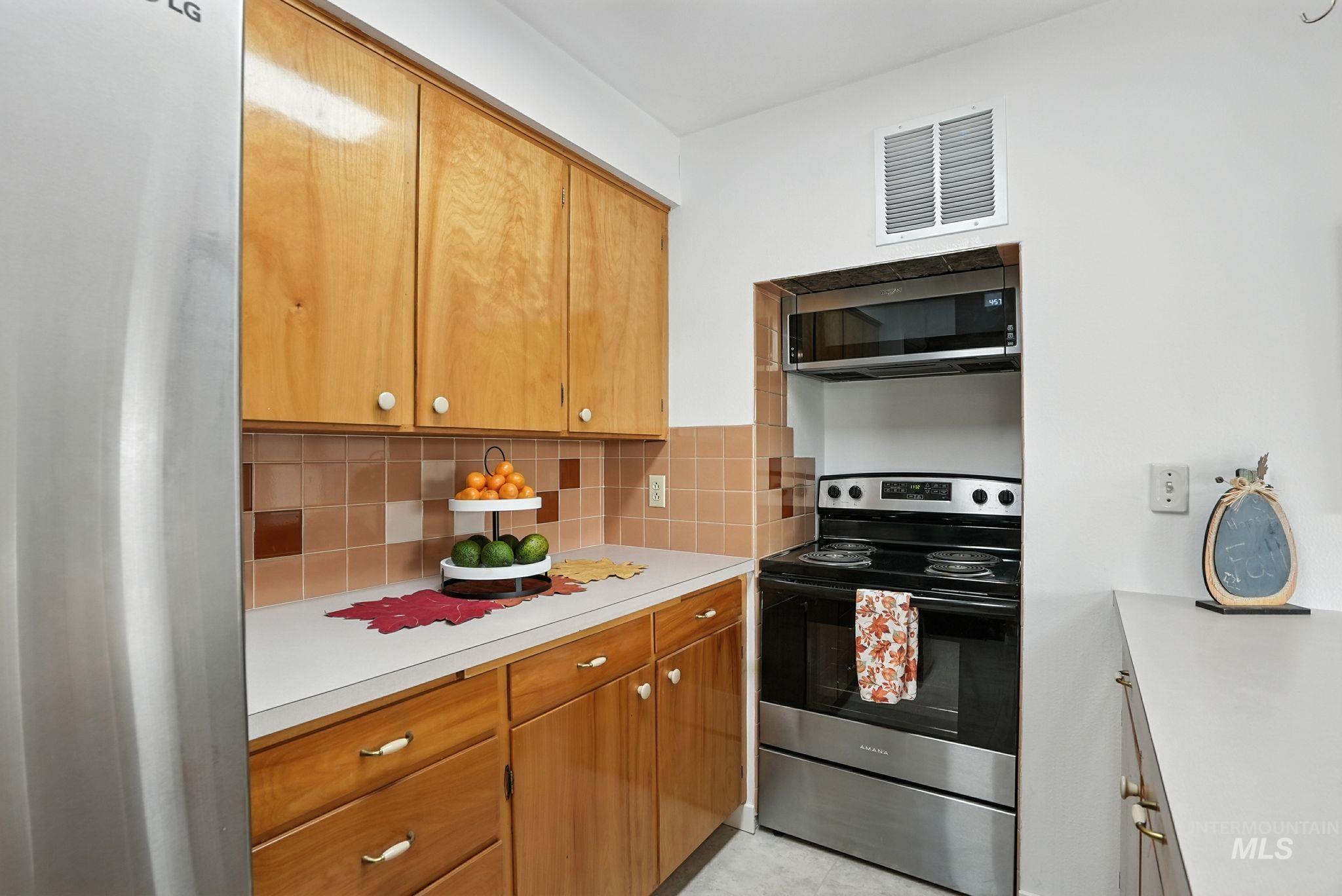 Kitchen featuring appliances with stainless steel finishes, light countertops, backsplash, brown cabinets, and light tile patterned floors