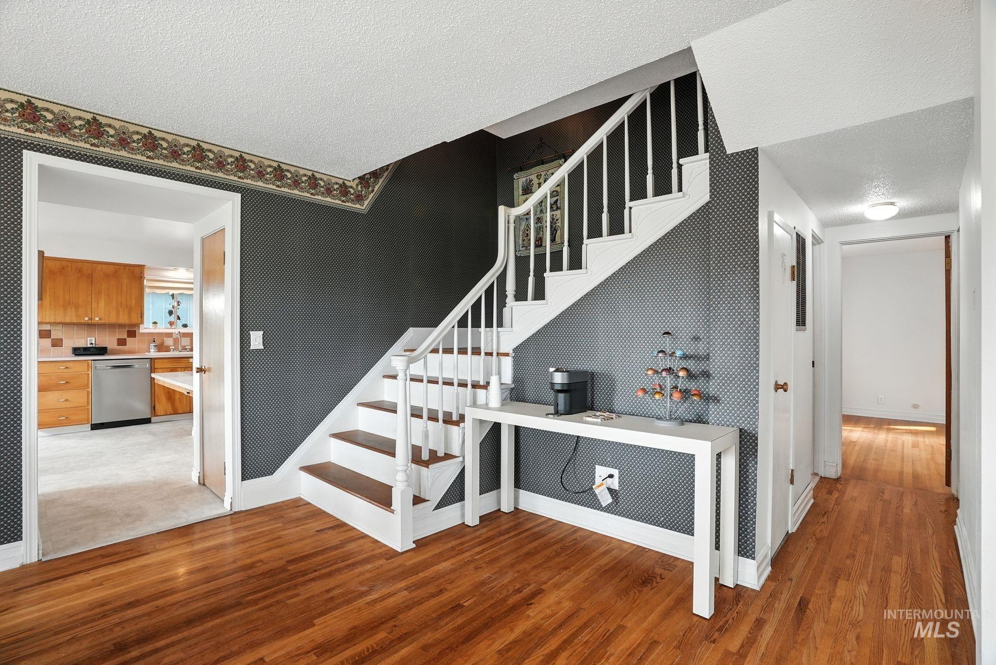 Staircase with a textured ceiling, wood finished floors, and wallpapered walls