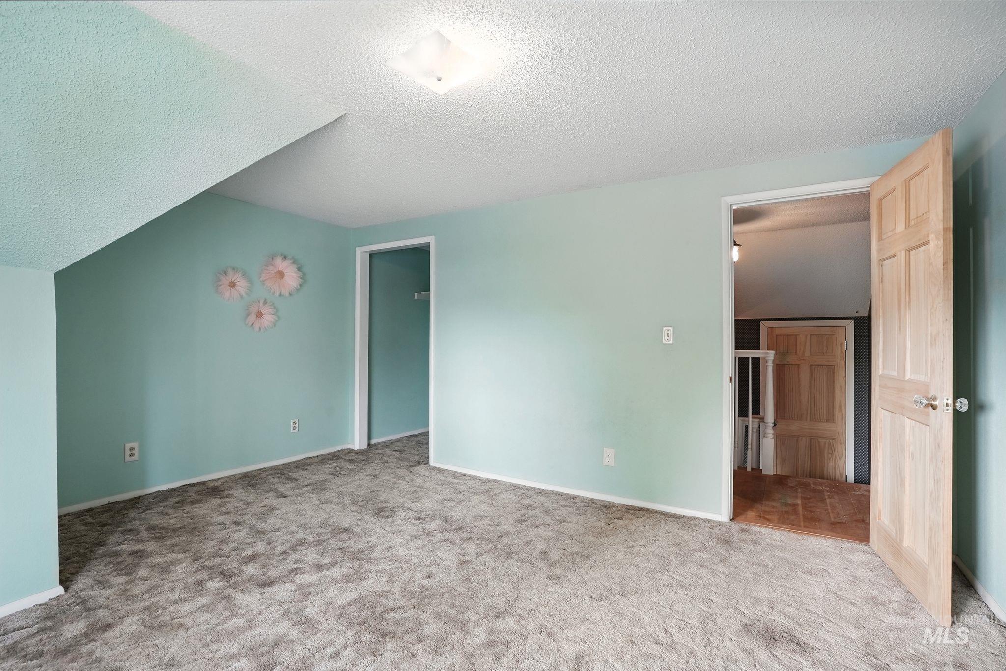 Unfurnished bedroom with a textured ceiling, carpet floors, and lofted ceiling