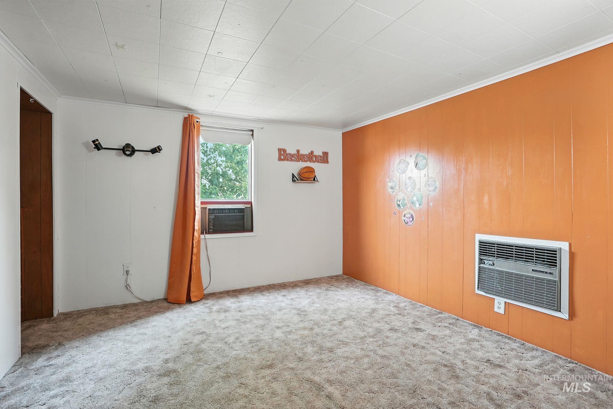 Carpeted empty room featuring ornamental molding, wooden walls, and heating unit