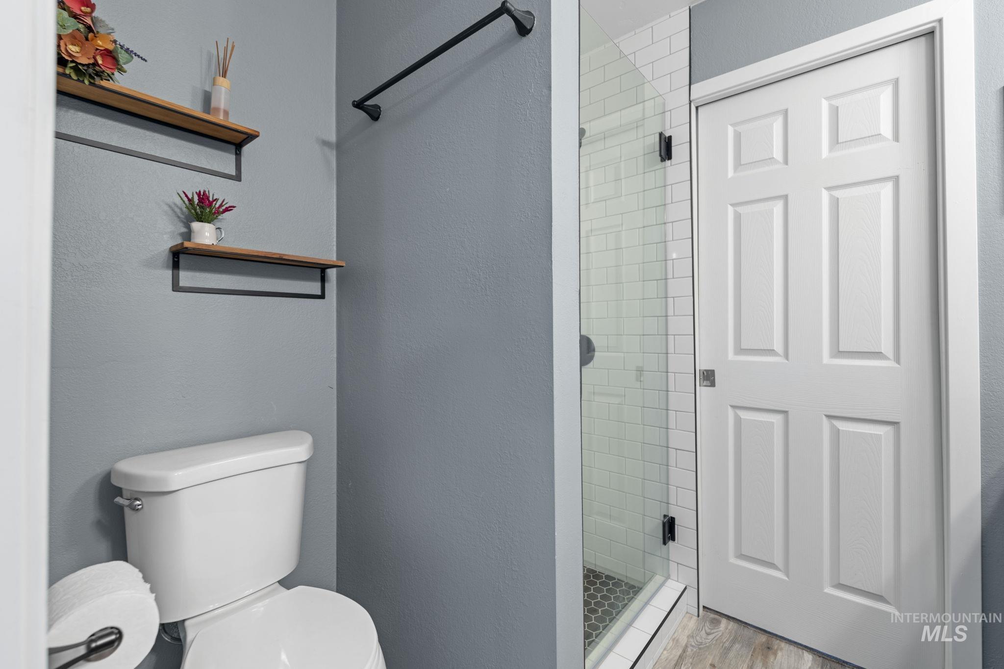 Bathroom with a shower stall, a textured wall, and wood finished floors