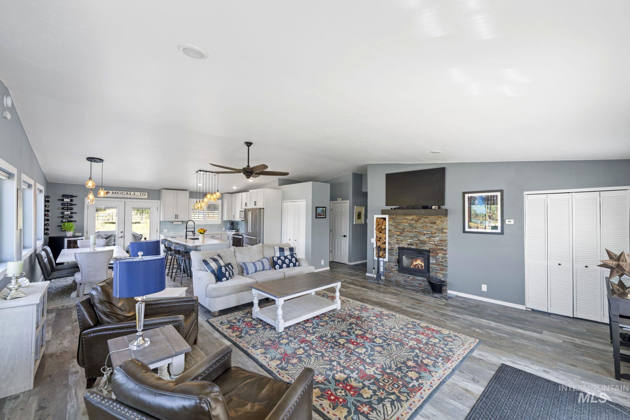 Living room featuring dark wood finished floors, a ceiling fan, and a stone fireplace