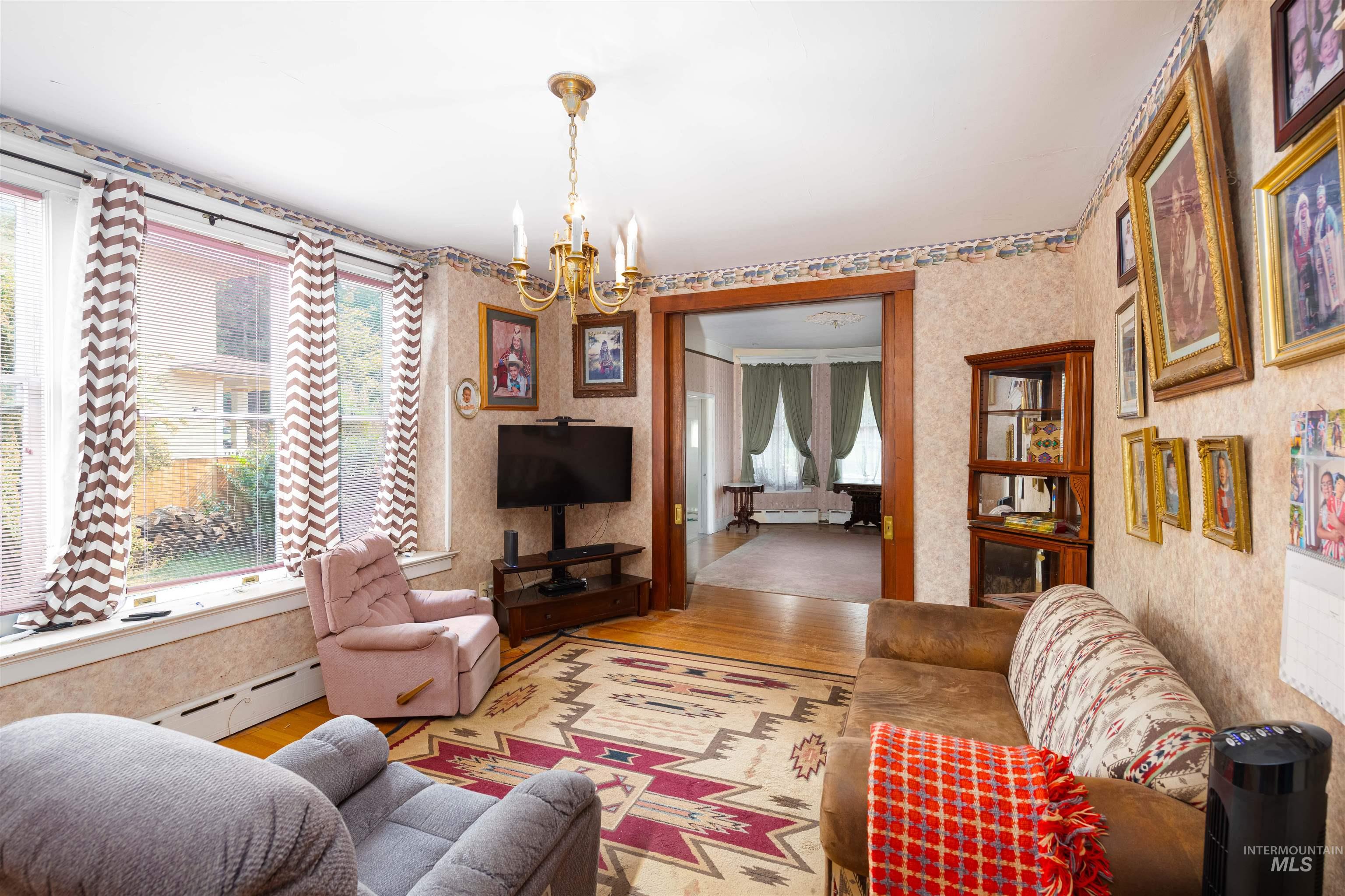 Living room with wood finished floors, a chandelier, baseboard heating, and wallpapered walls