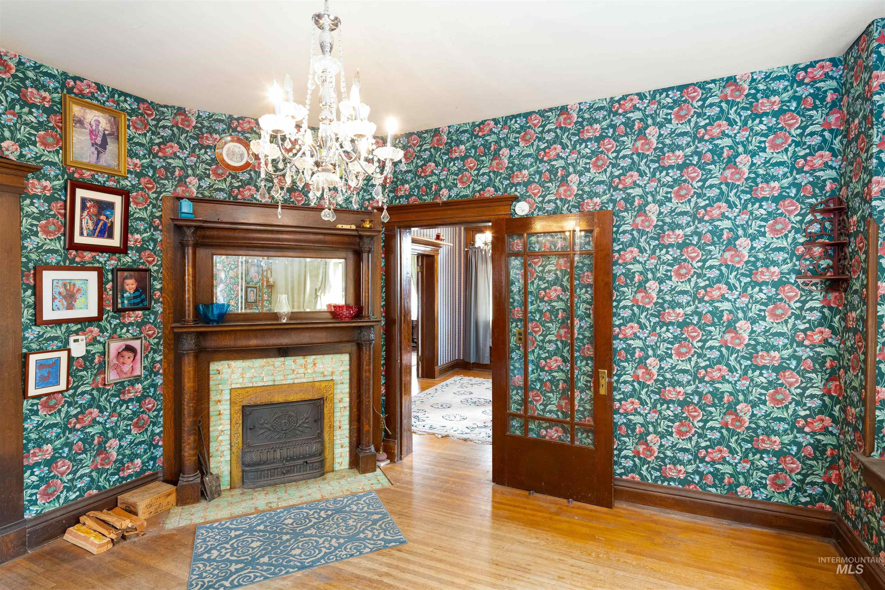 Unfurnished living room with wallpapered walls, wood finished floors, a chandelier, and a fireplace with flush hearth