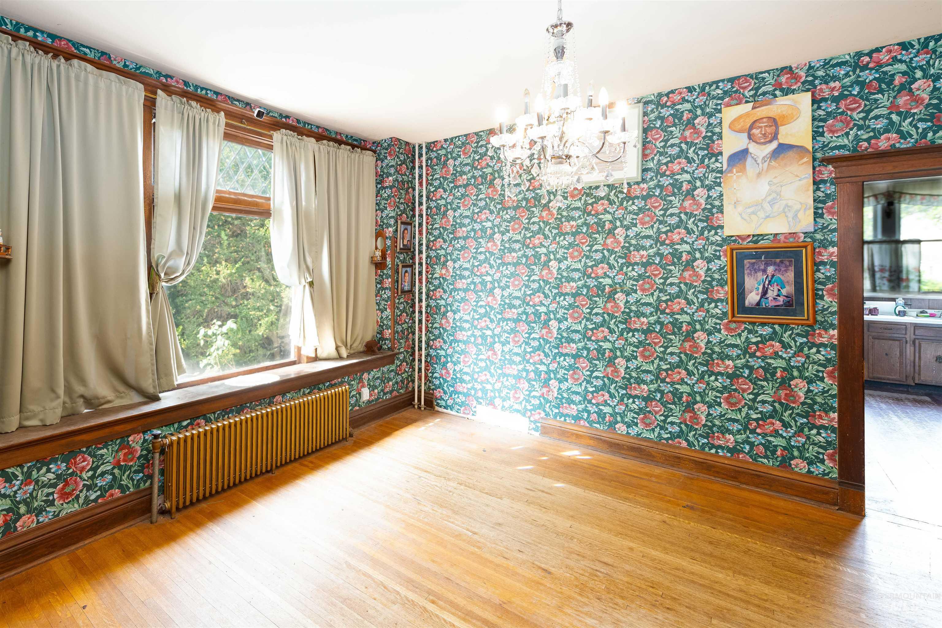 Spare room featuring wallpapered walls, light wood-style floors, radiator, and a chandelier