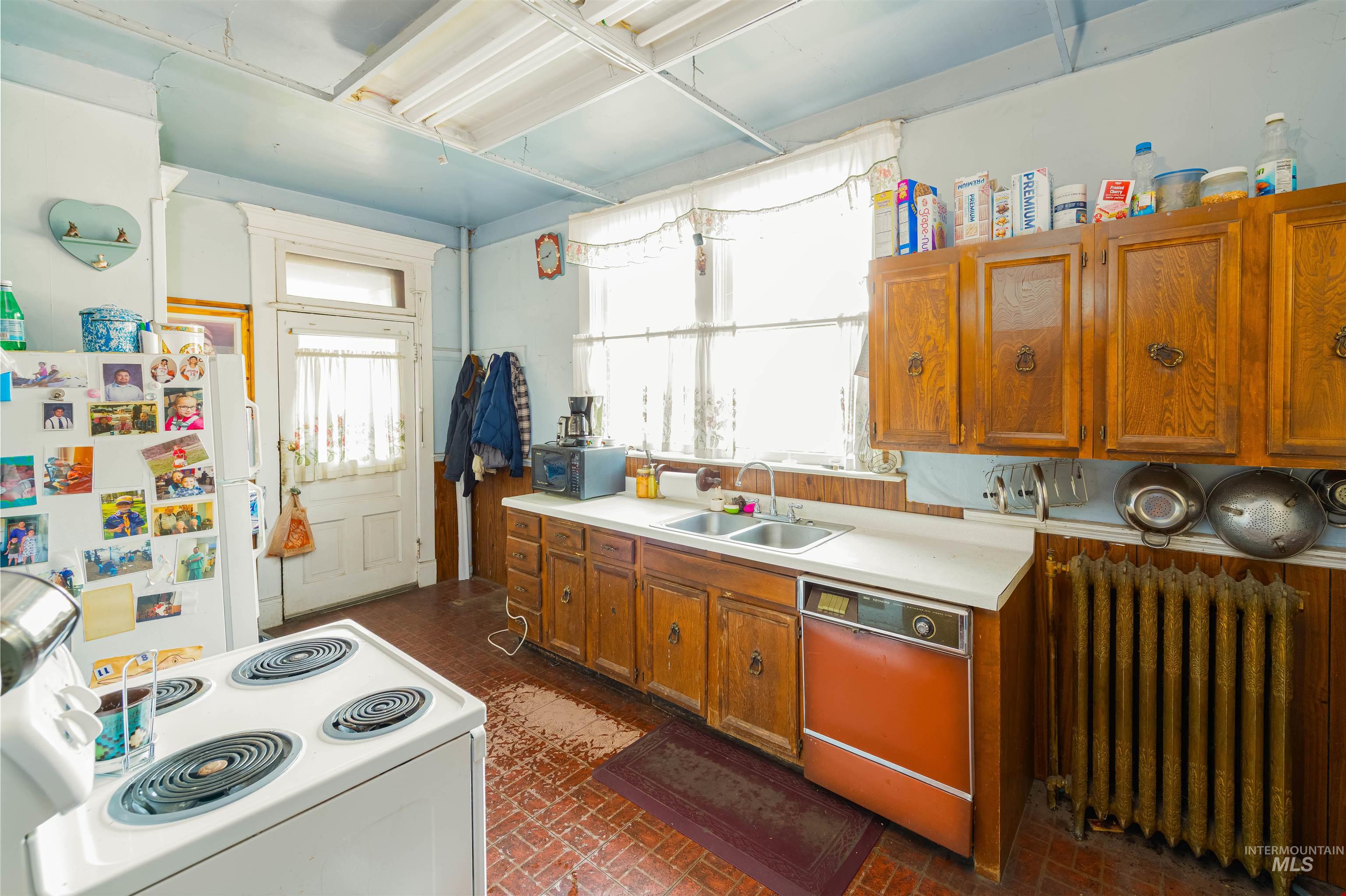 Kitchen featuring radiator heating unit, light countertops, white appliances, brick patterned flooring, and brown cabinets