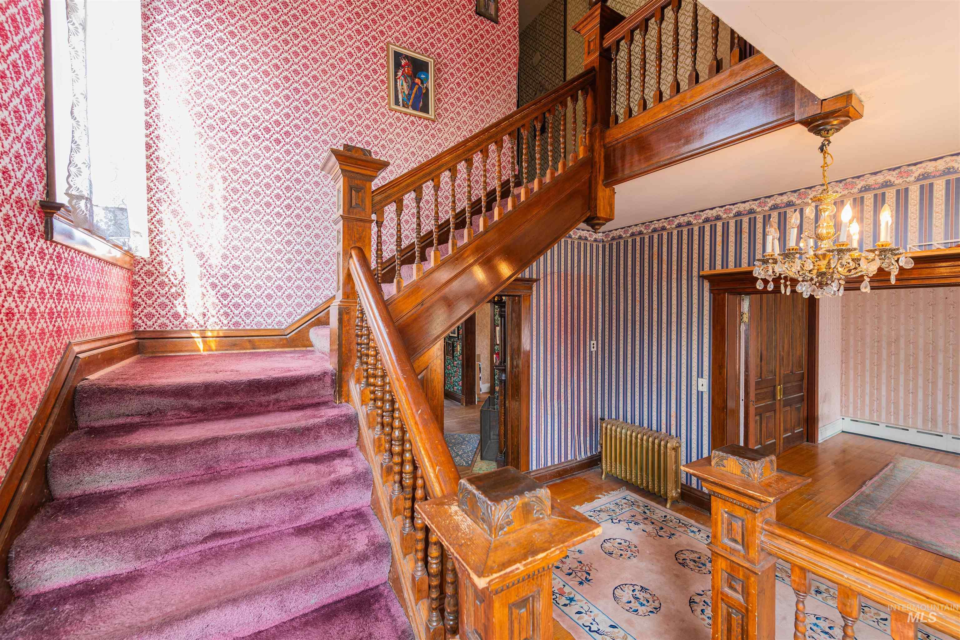 Stairway featuring wallpapered walls, radiator, and a chandelier