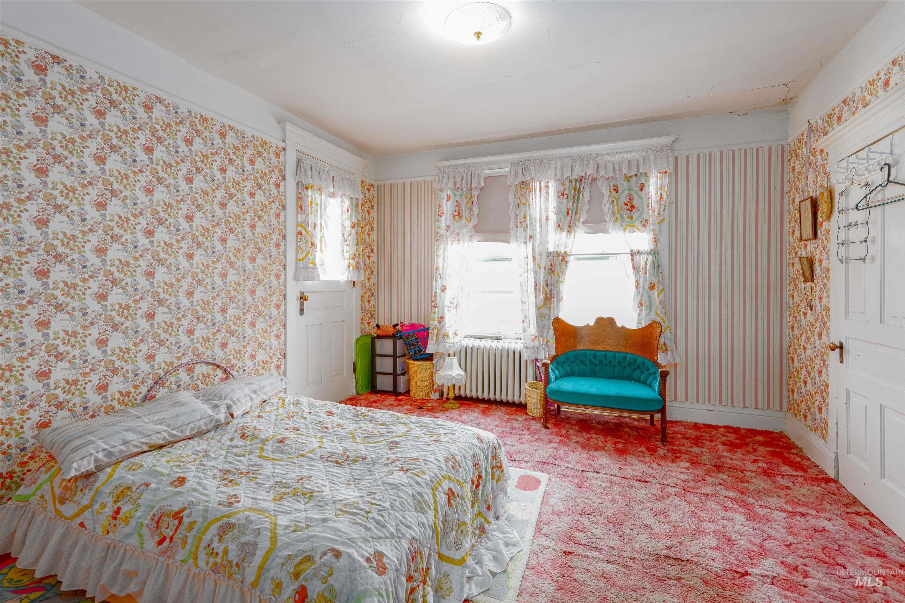 Carpeted bedroom with wallpapered walls and radiator heating unit