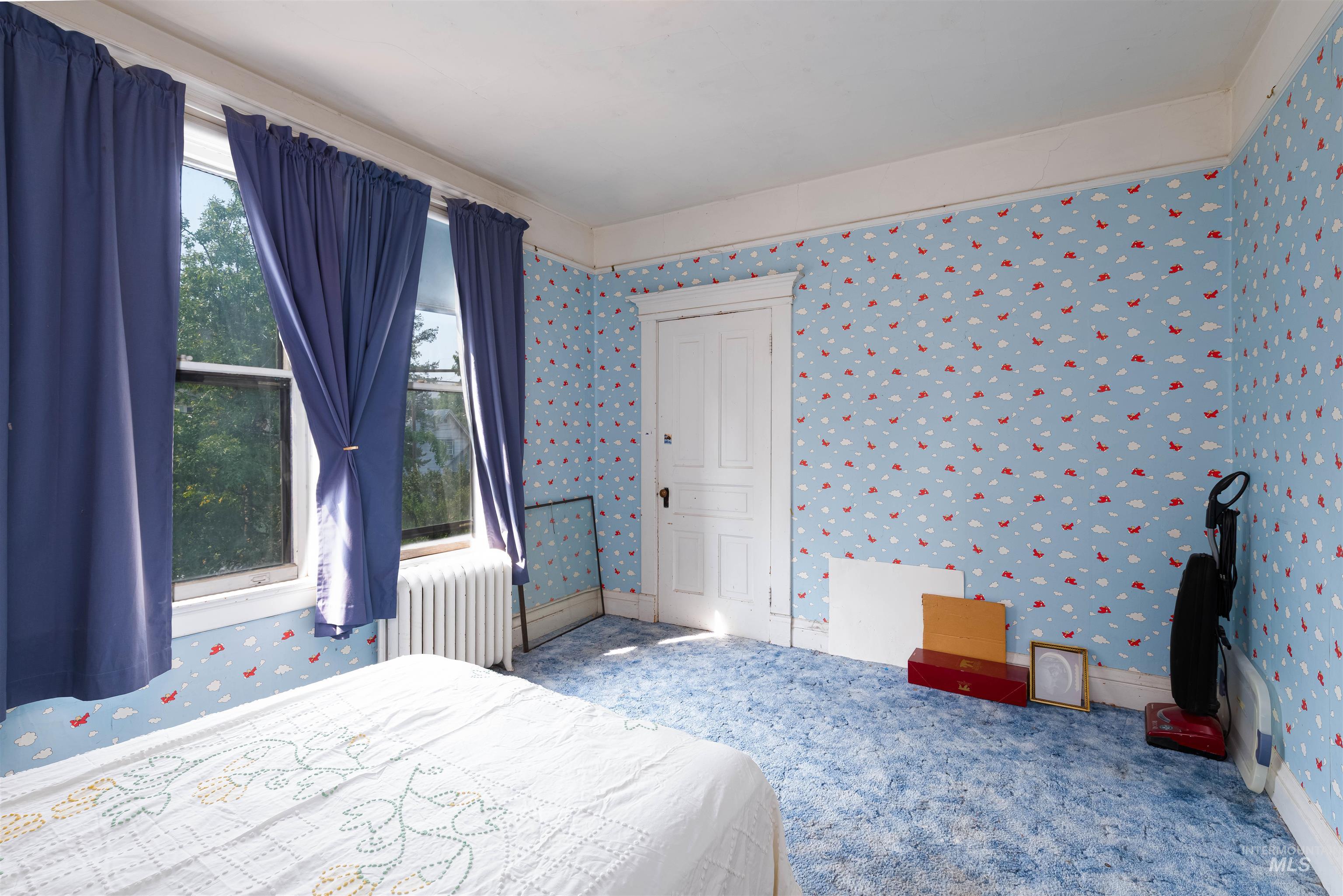 Bedroom with wallpapered walls, radiator, and carpet floors