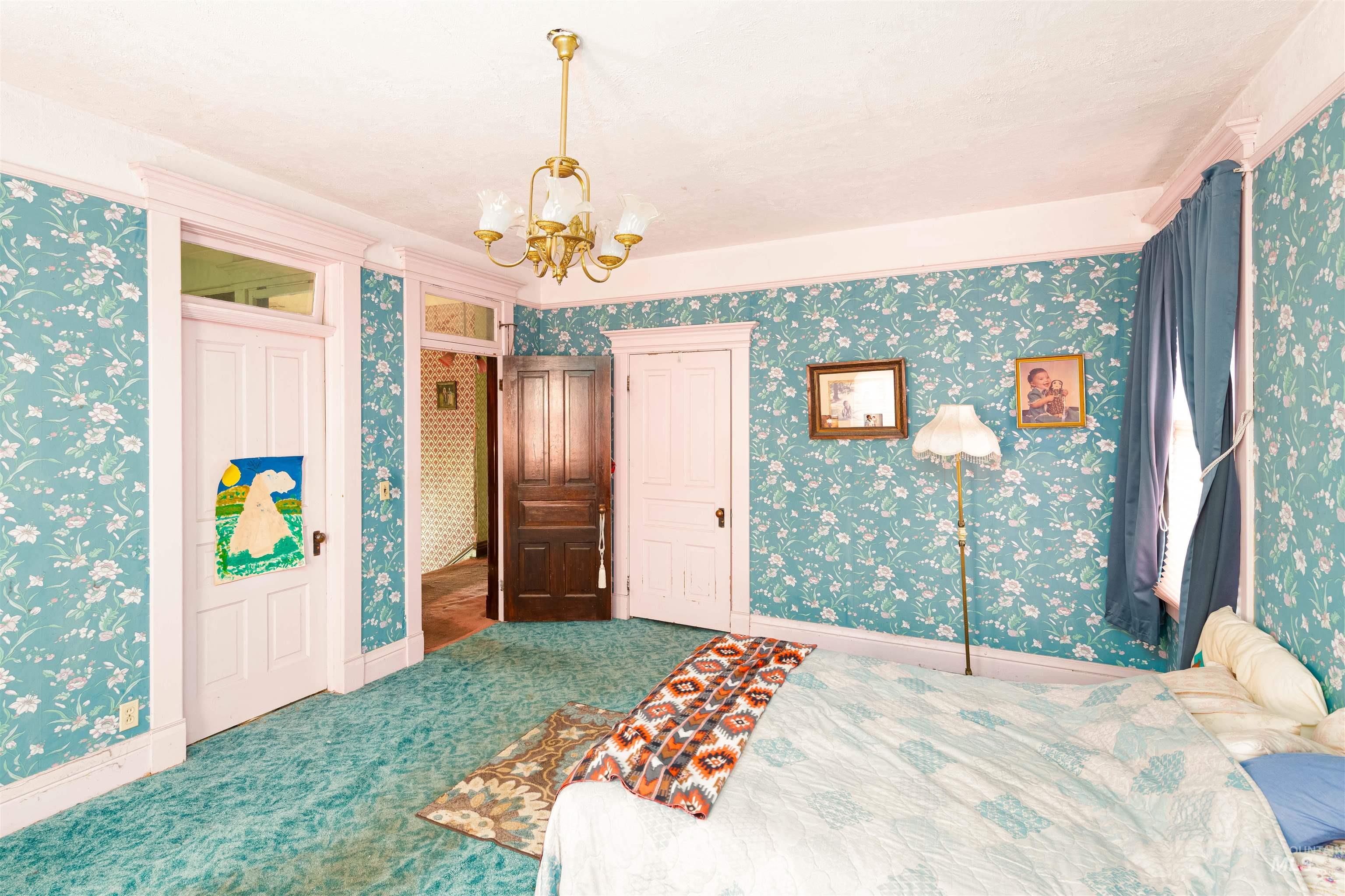 Carpeted bedroom featuring wallpapered walls, a chandelier, and a closet