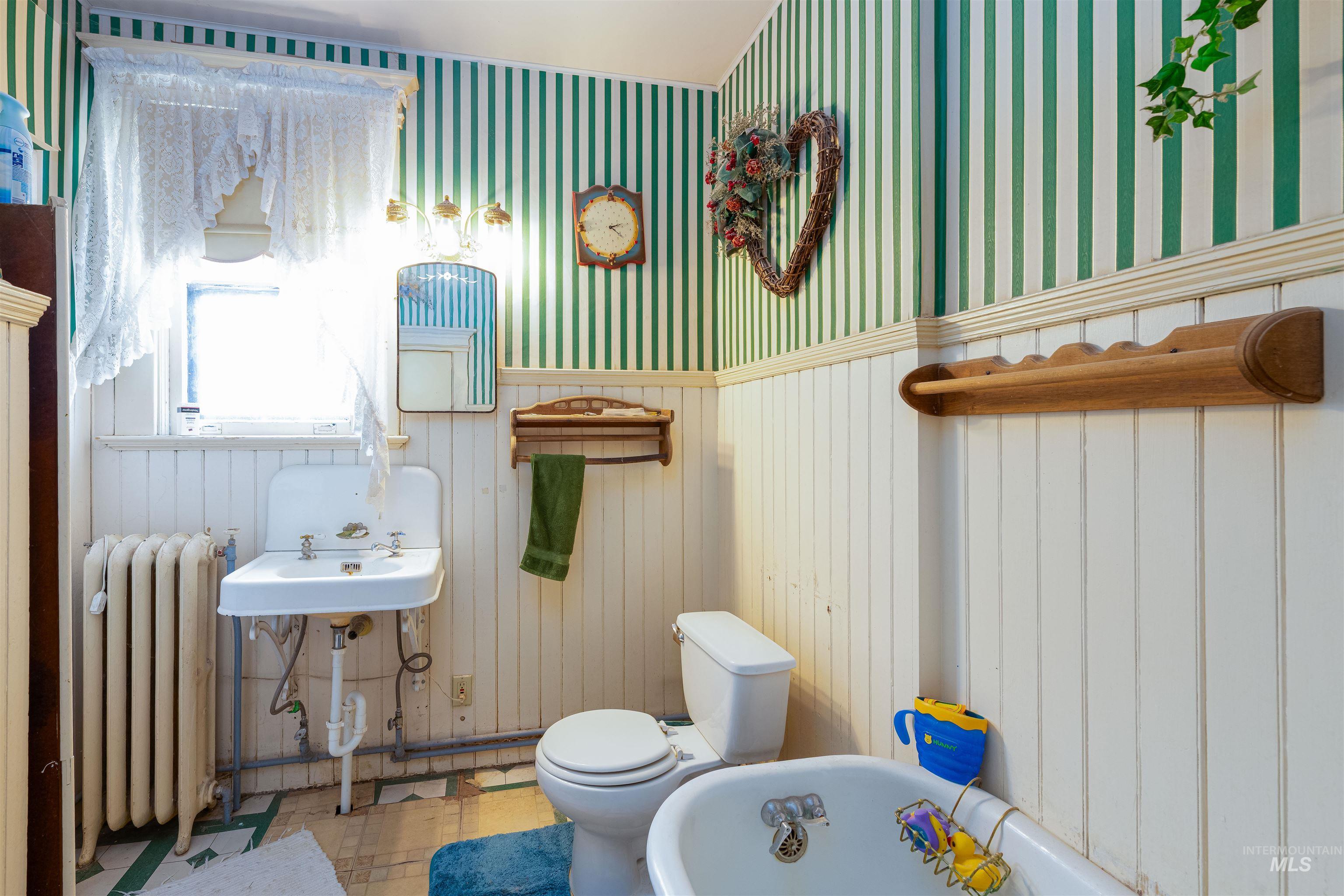 Bathroom featuring a freestanding bath, radiator heating unit, wallpapered walls, wainscoting, and tile patterned floors
