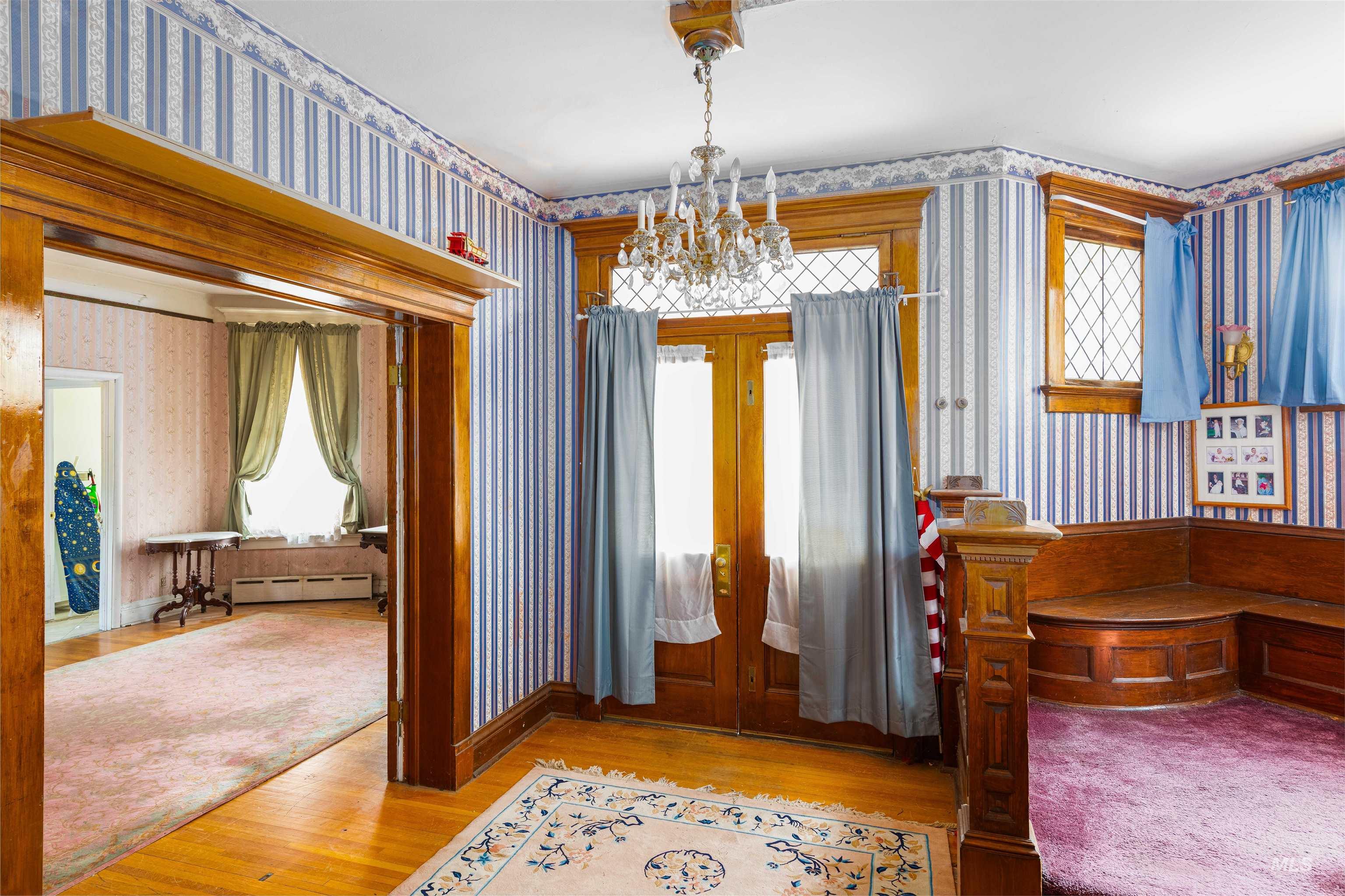 Foyer with wallpapered walls, light wood finished floors, a chandelier, french doors, and baseboard heating