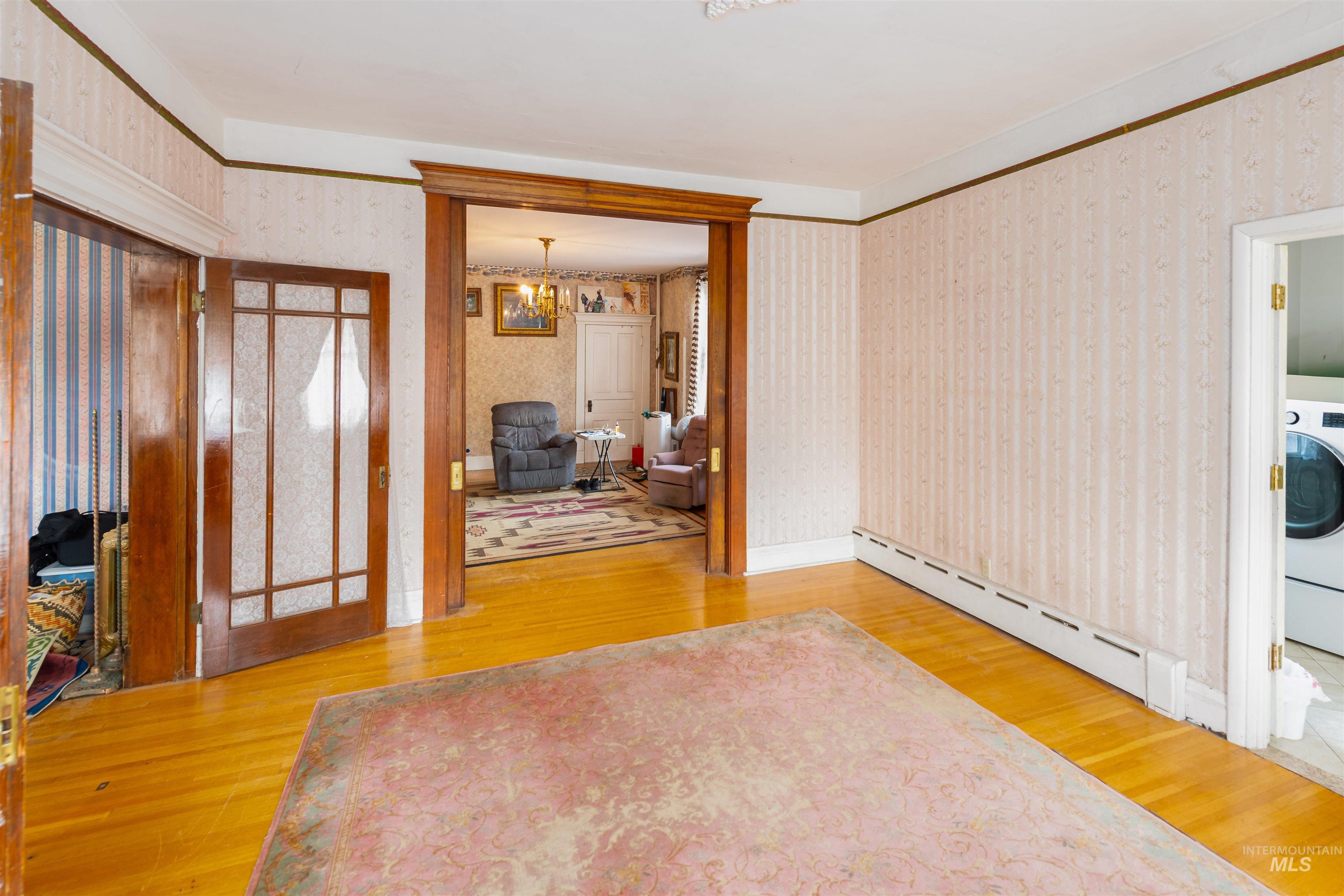 Entrance foyer with a baseboard heating unit, light wood-style floors, washer / dryer, wallpapered walls, and a chandelier