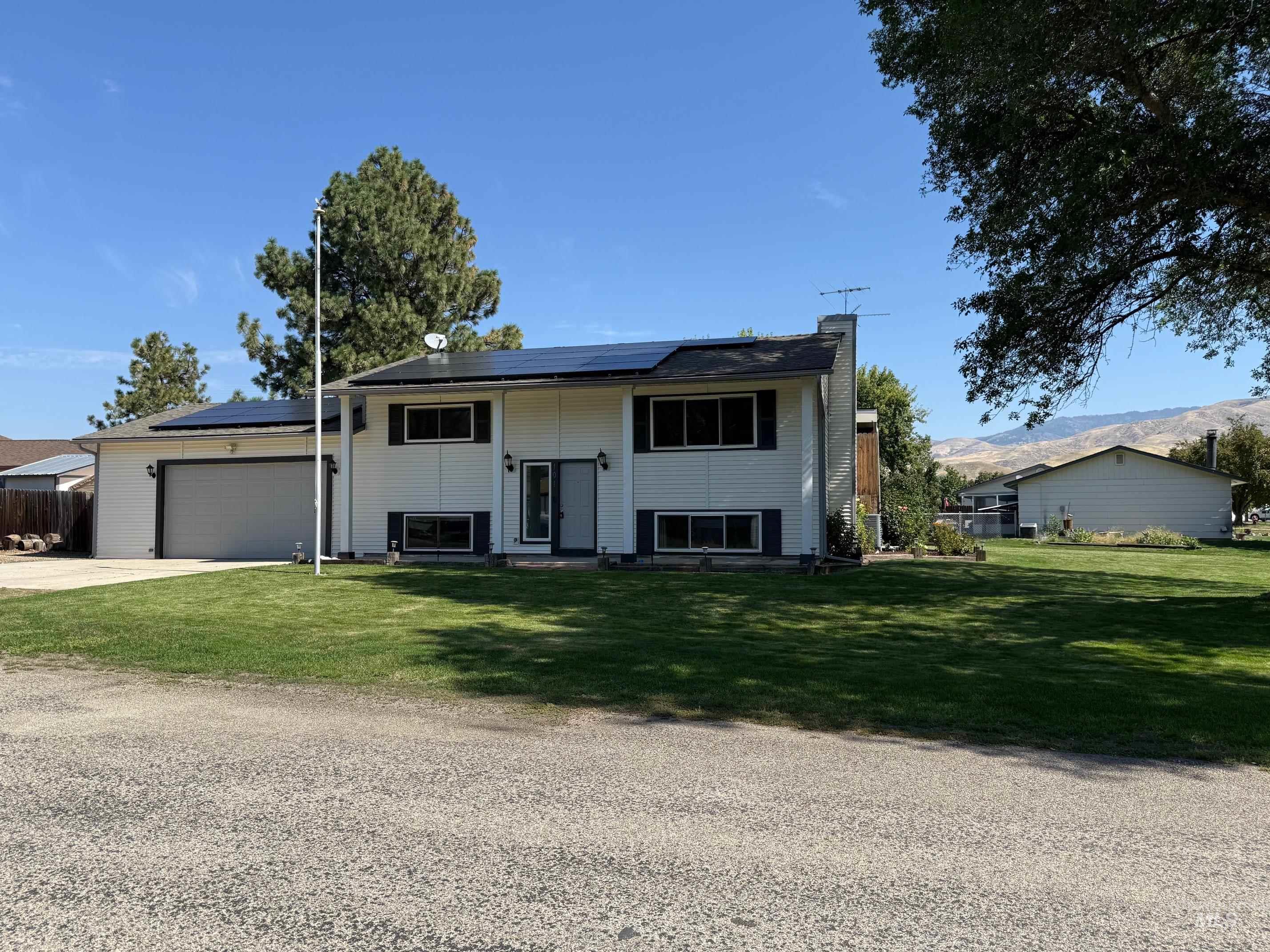 Bi-level home featuring roof mounted solar panels, a front lawn, driveway, and a chimney