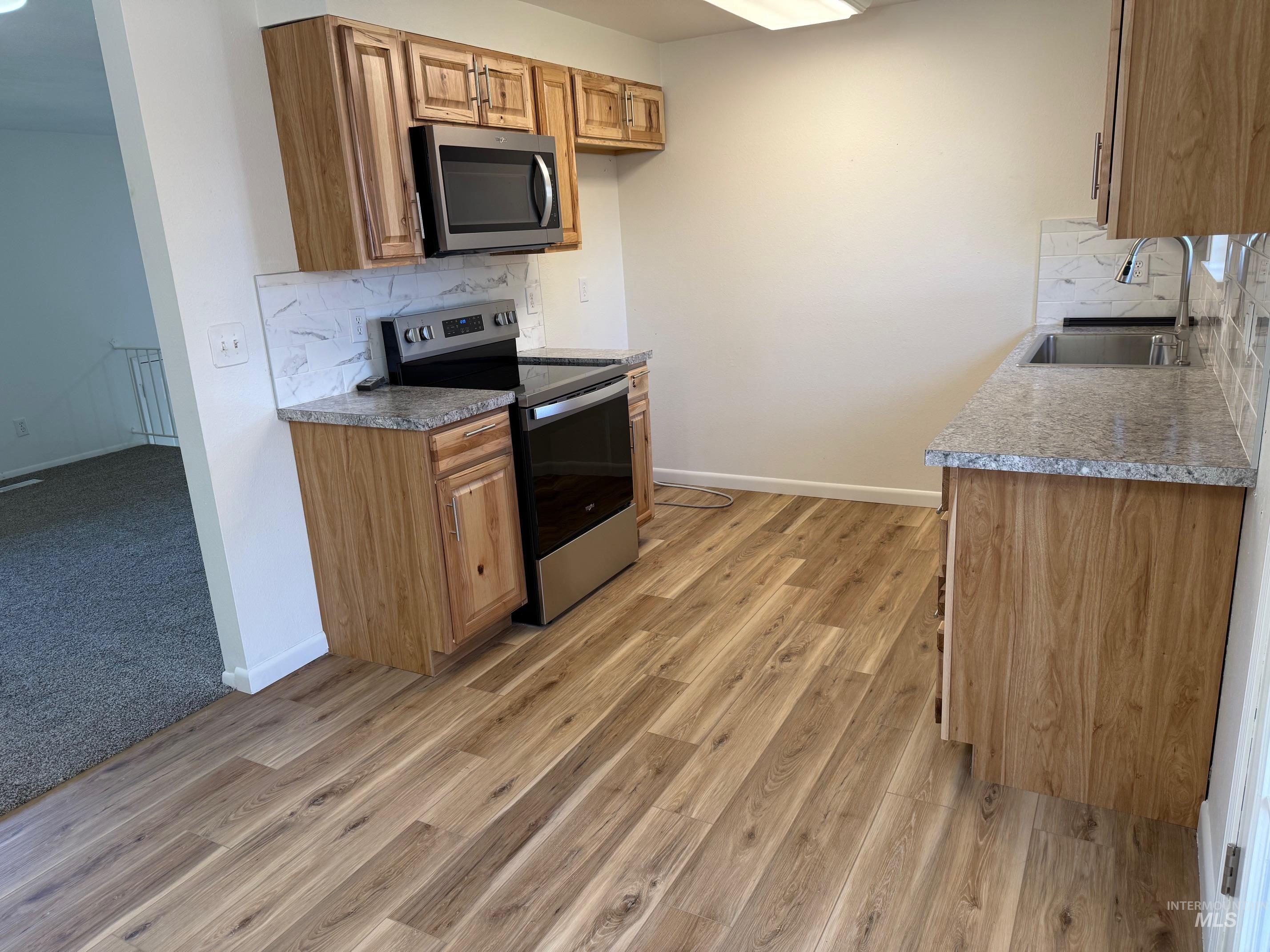 Kitchen with backsplash, stainless steel appliances, light wood-style flooring, and brown cabinetry