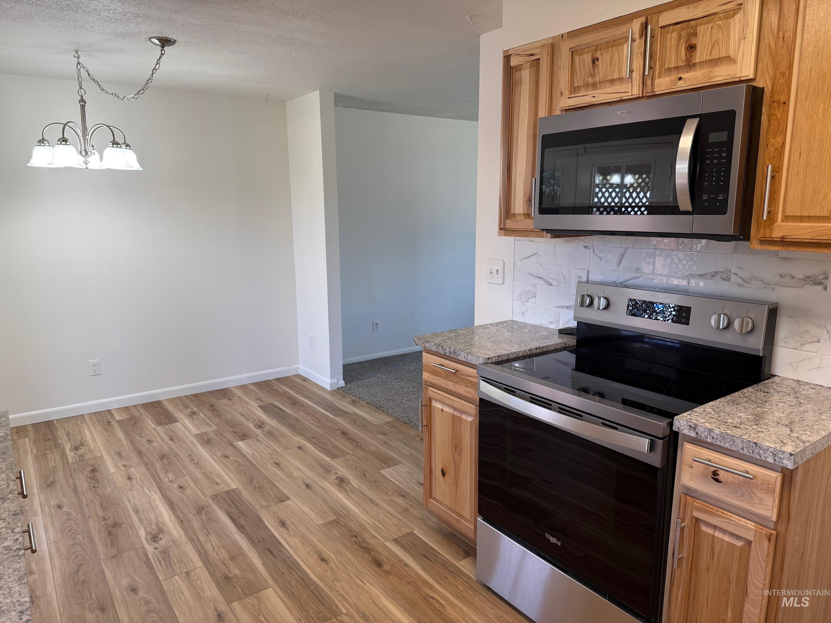 Kitchen with appliances with stainless steel finishes, backsplash, light wood-style floors, pendant lighting, and a chandelier
