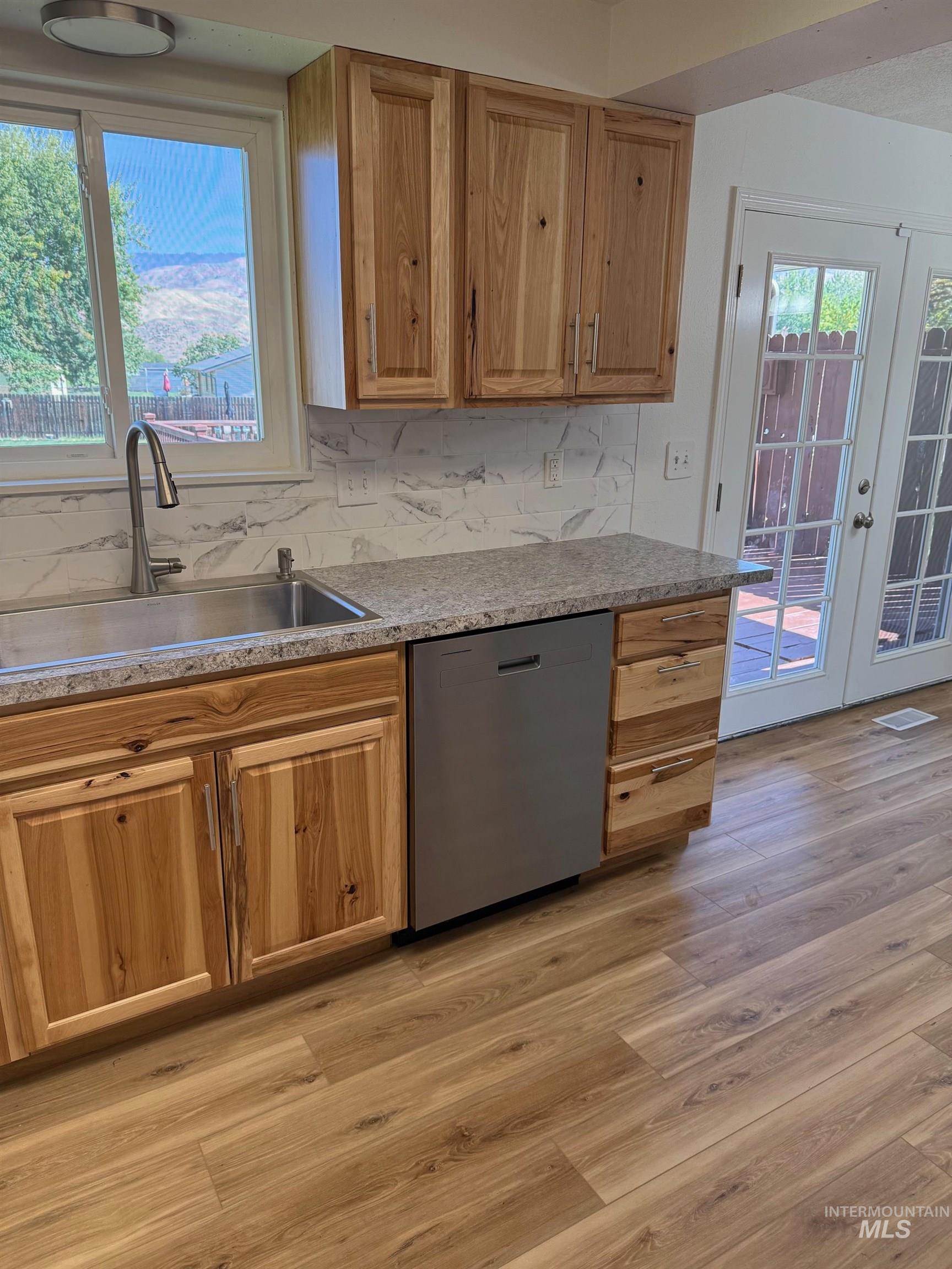 Kitchen with decorative backsplash, dishwasher, light wood finished floors, french doors, and brown cabinetry