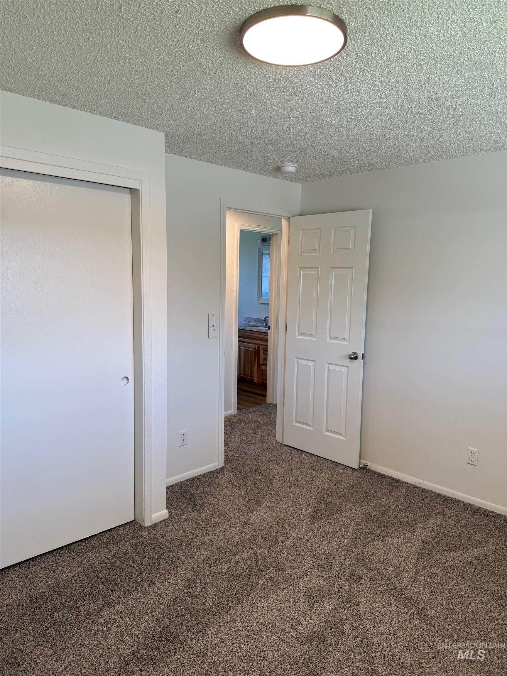 Unfurnished bedroom with dark carpet, a textured ceiling, and a closet