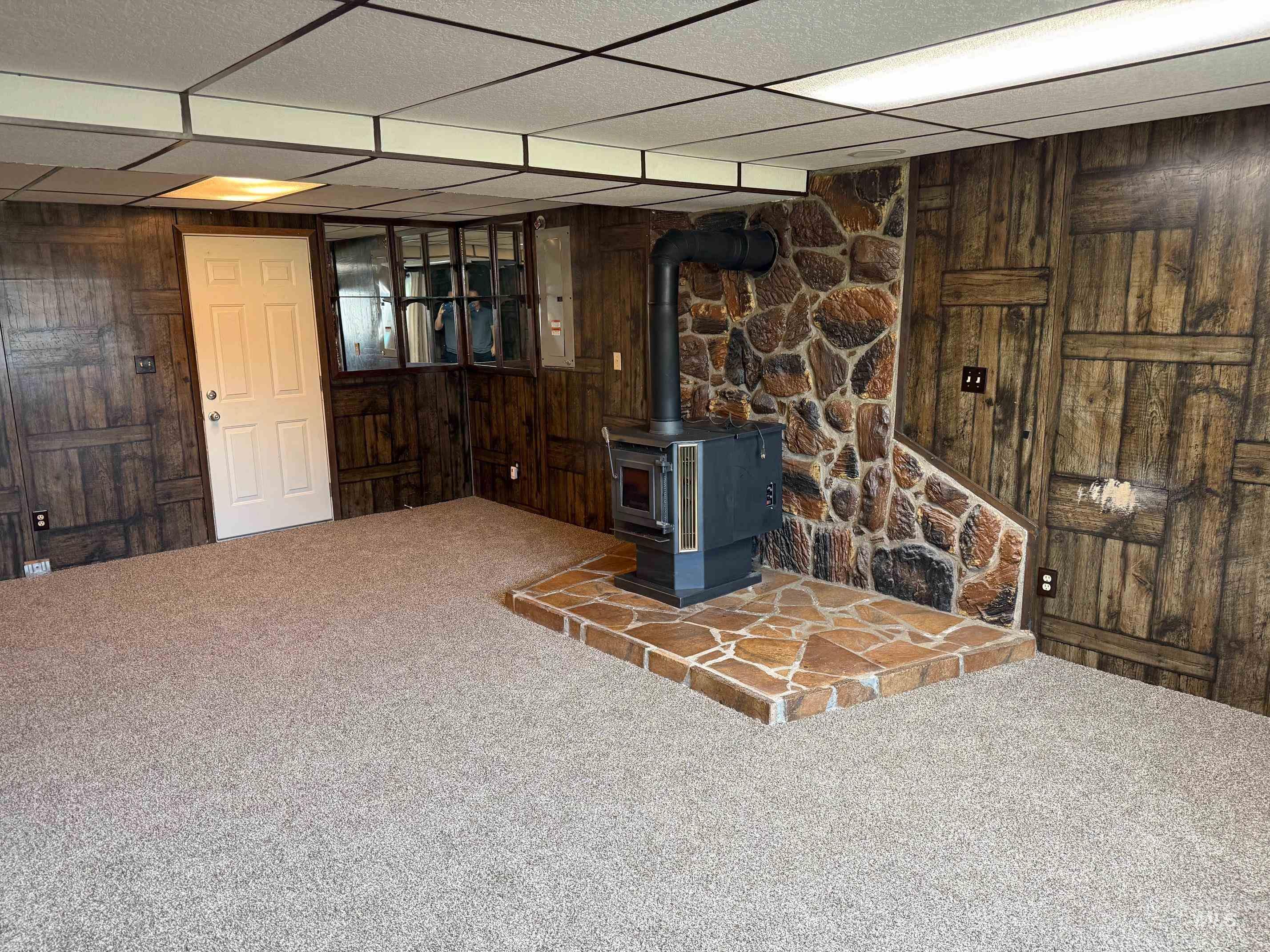 Unfurnished living room with a drop ceiling, a wood stove, carpet floors, and wooden walls