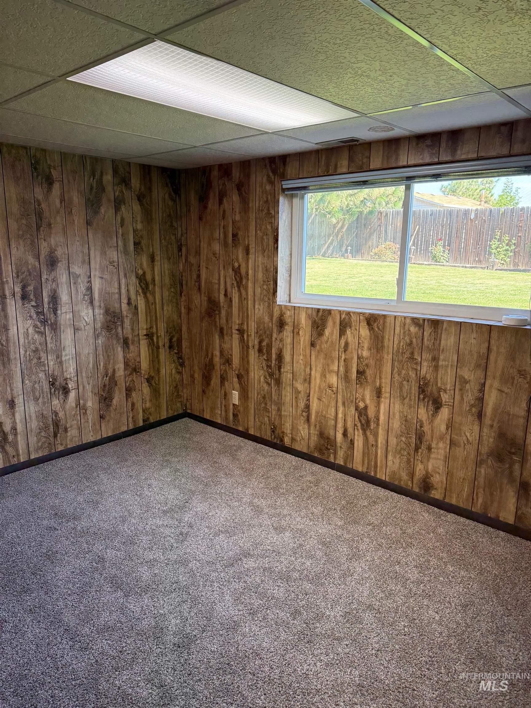 Carpeted spare room with a drop ceiling and wood walls