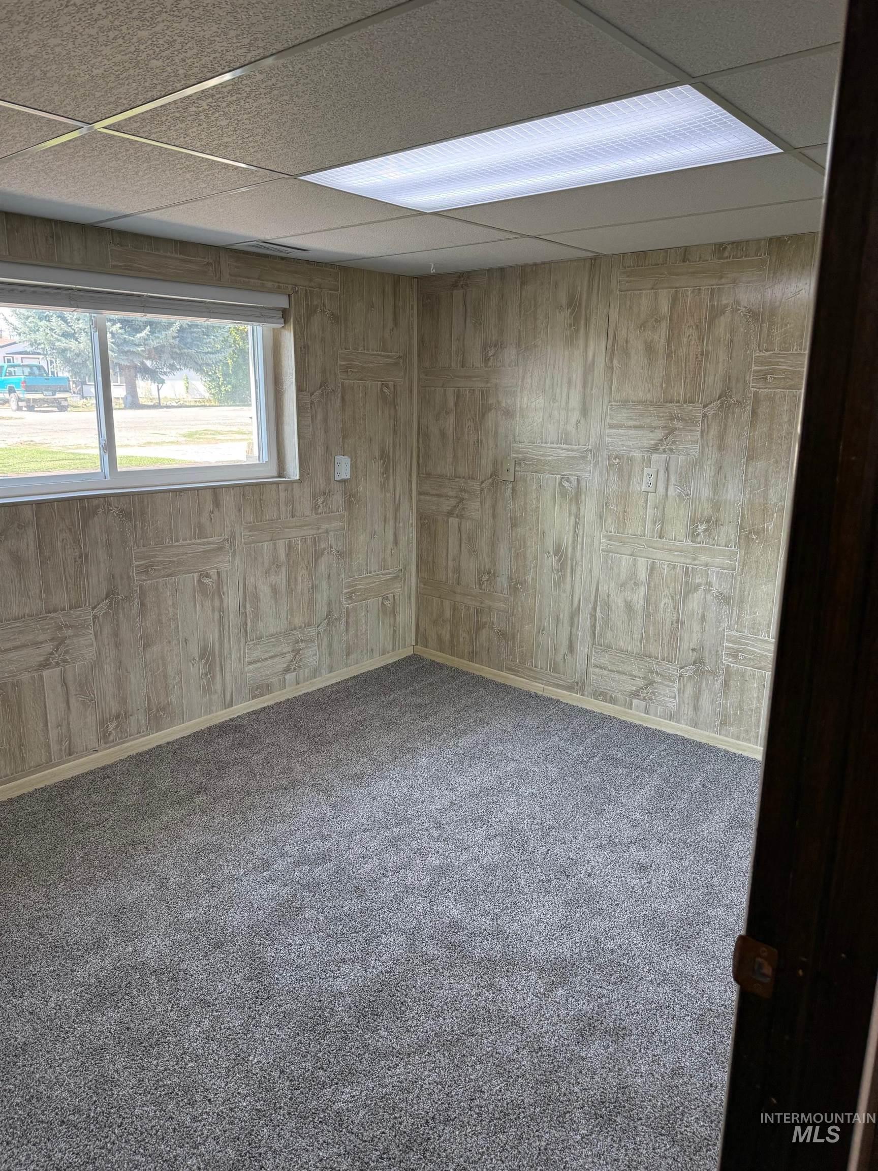 Carpeted empty room with wooden walls and a paneled ceiling