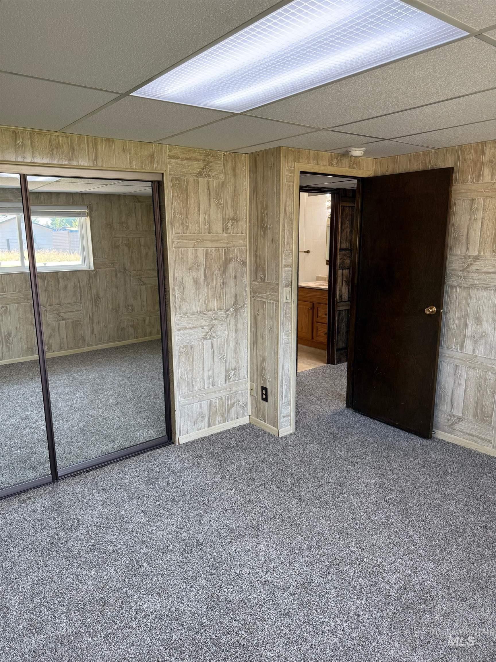 Unfurnished bedroom with wooden walls, a drop ceiling, carpet floors, and a closet