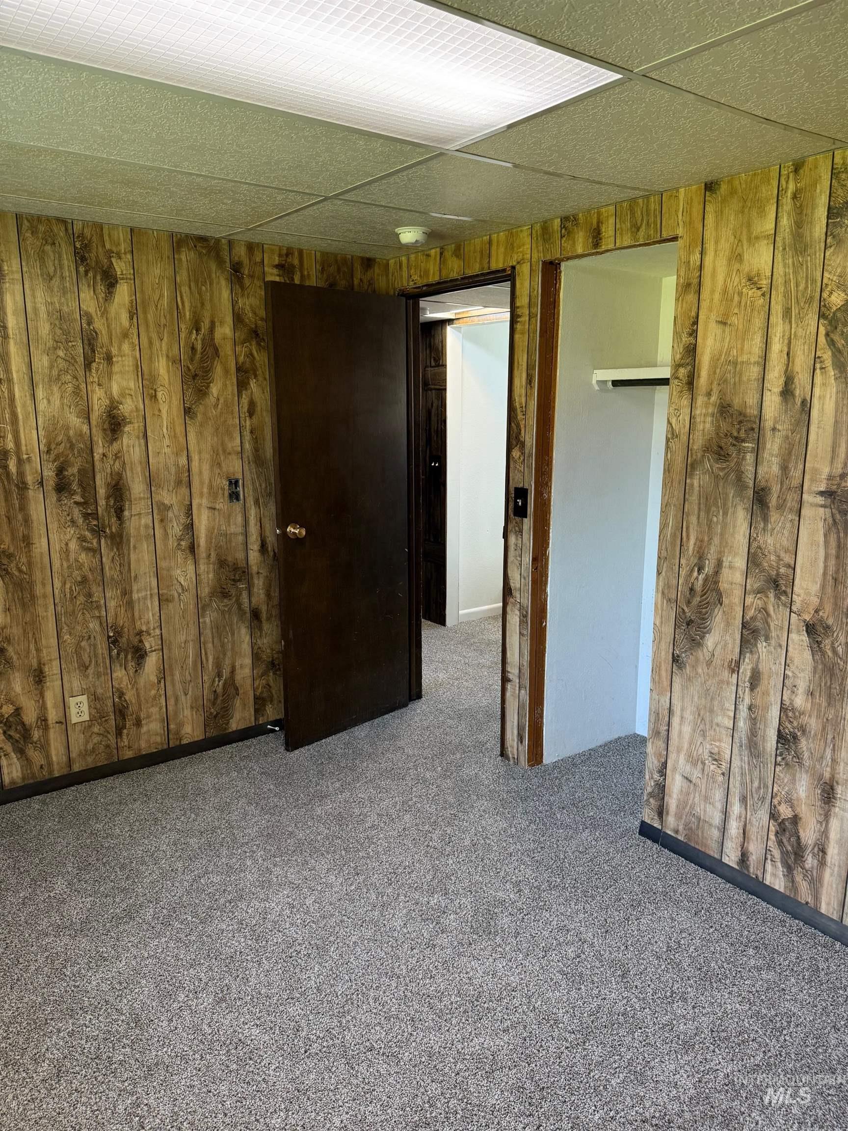 Unfurnished bedroom featuring wooden walls, carpet, and a drop ceiling