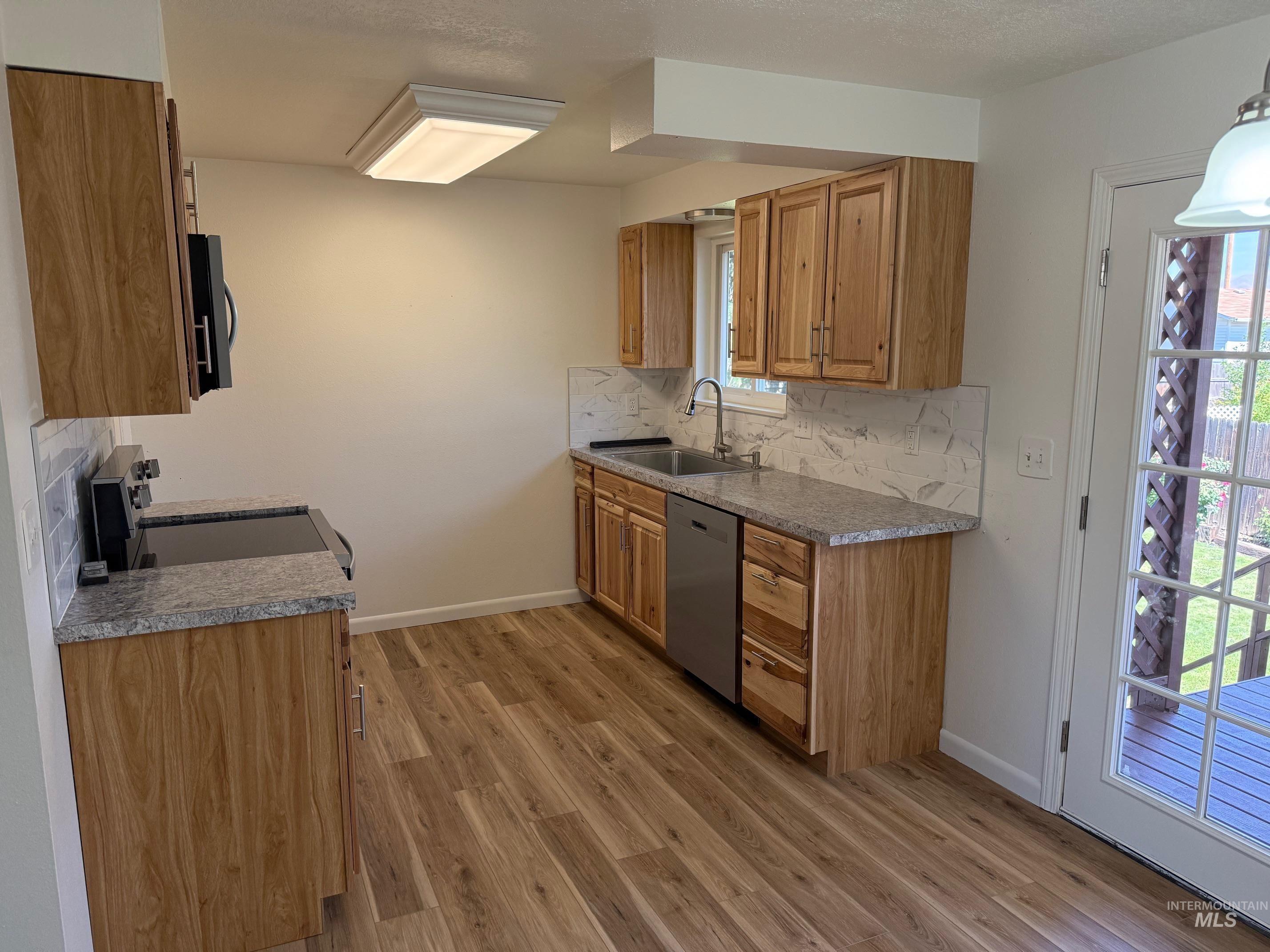 Kitchen with tasteful backsplash, appliances with stainless steel finishes, light wood-style flooring, brown cabinetry, and dark stone counters