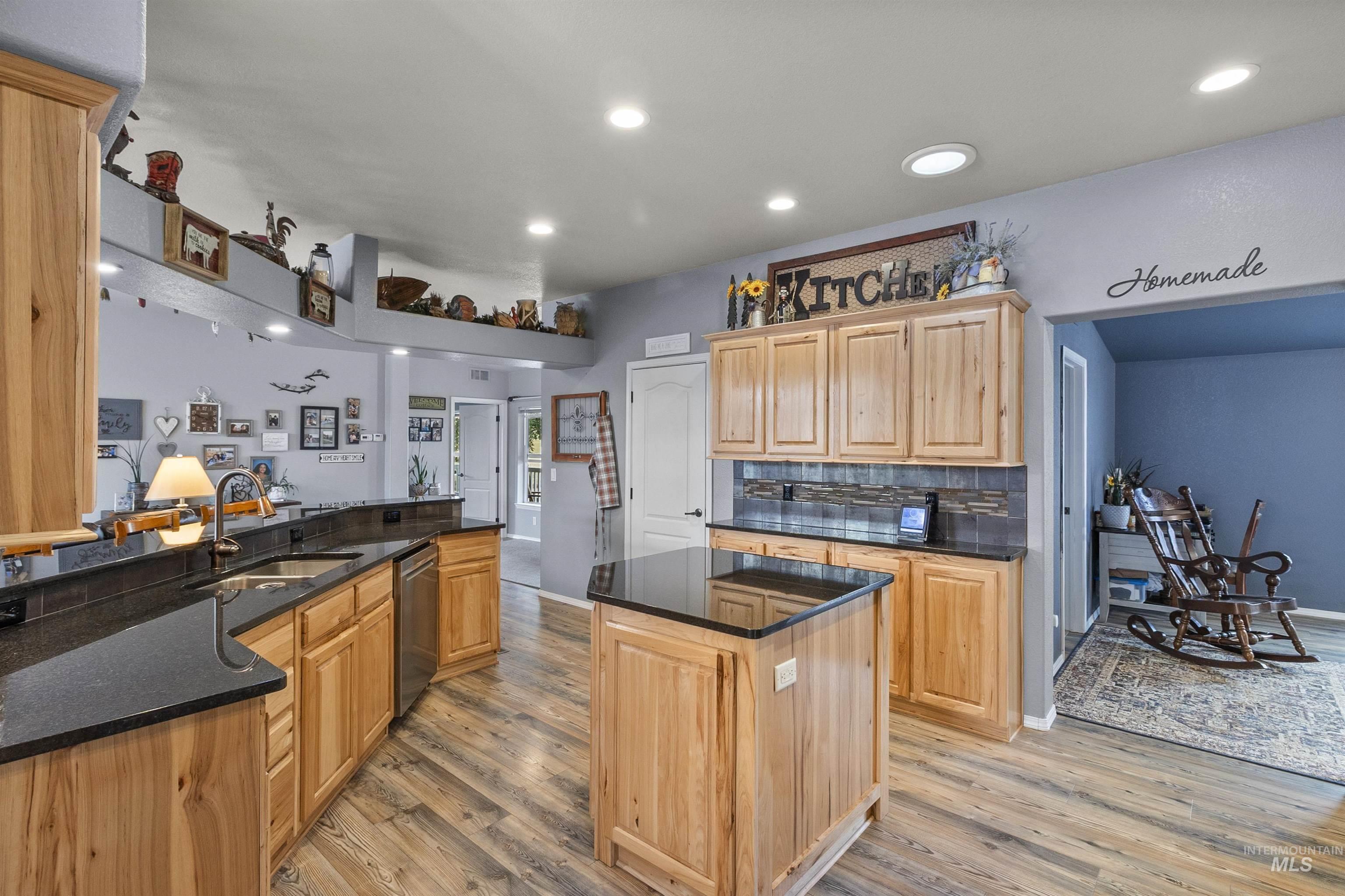 Kitchen featuring recessed lighting, decorative backsplash, a kitchen island, light wood-style flooring, and dark stone countertops