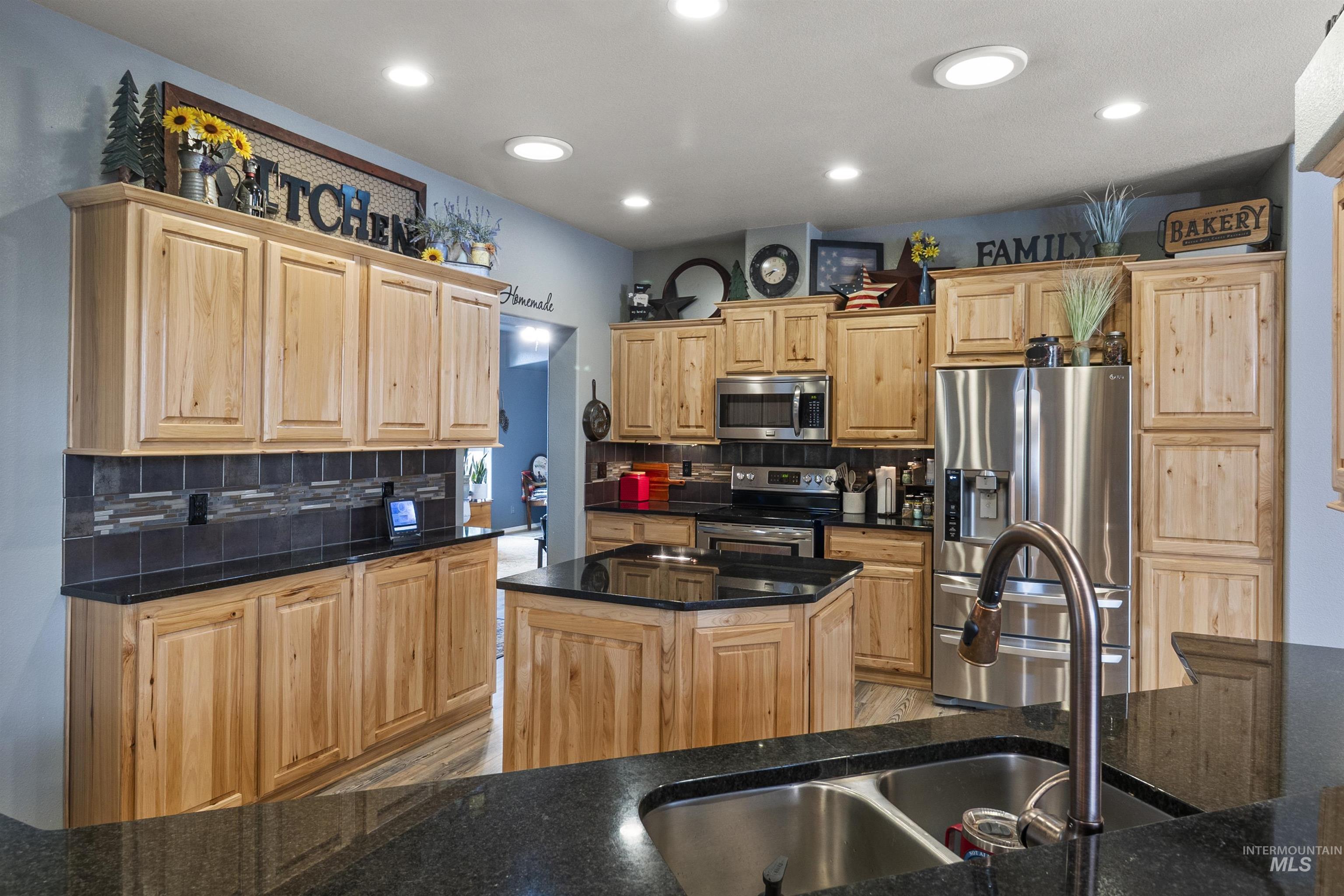 Kitchen with stainless steel appliances, decorative backsplash, light brown cabinetry, and recessed lighting