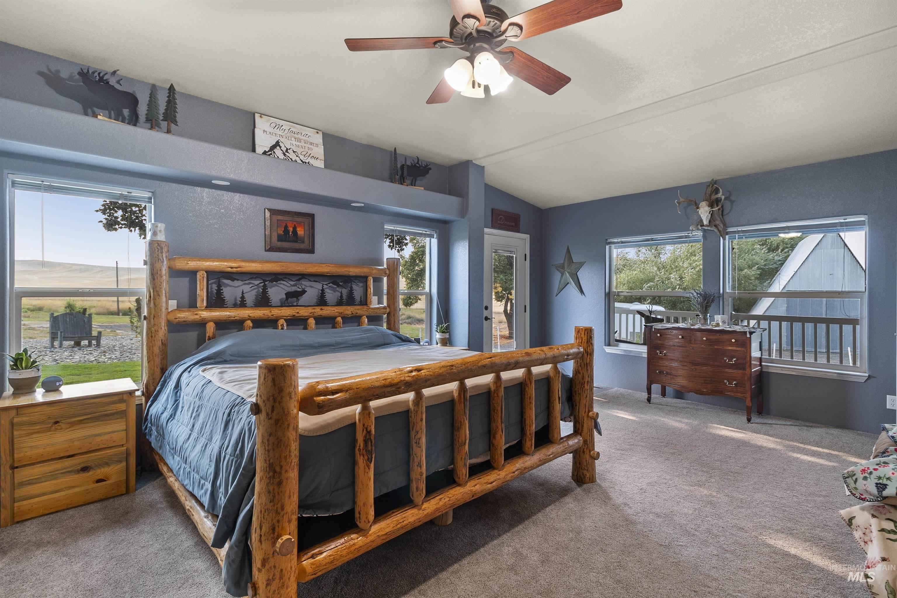 Carpeted bedroom featuring access to exterior, vaulted ceiling, and ceiling fan