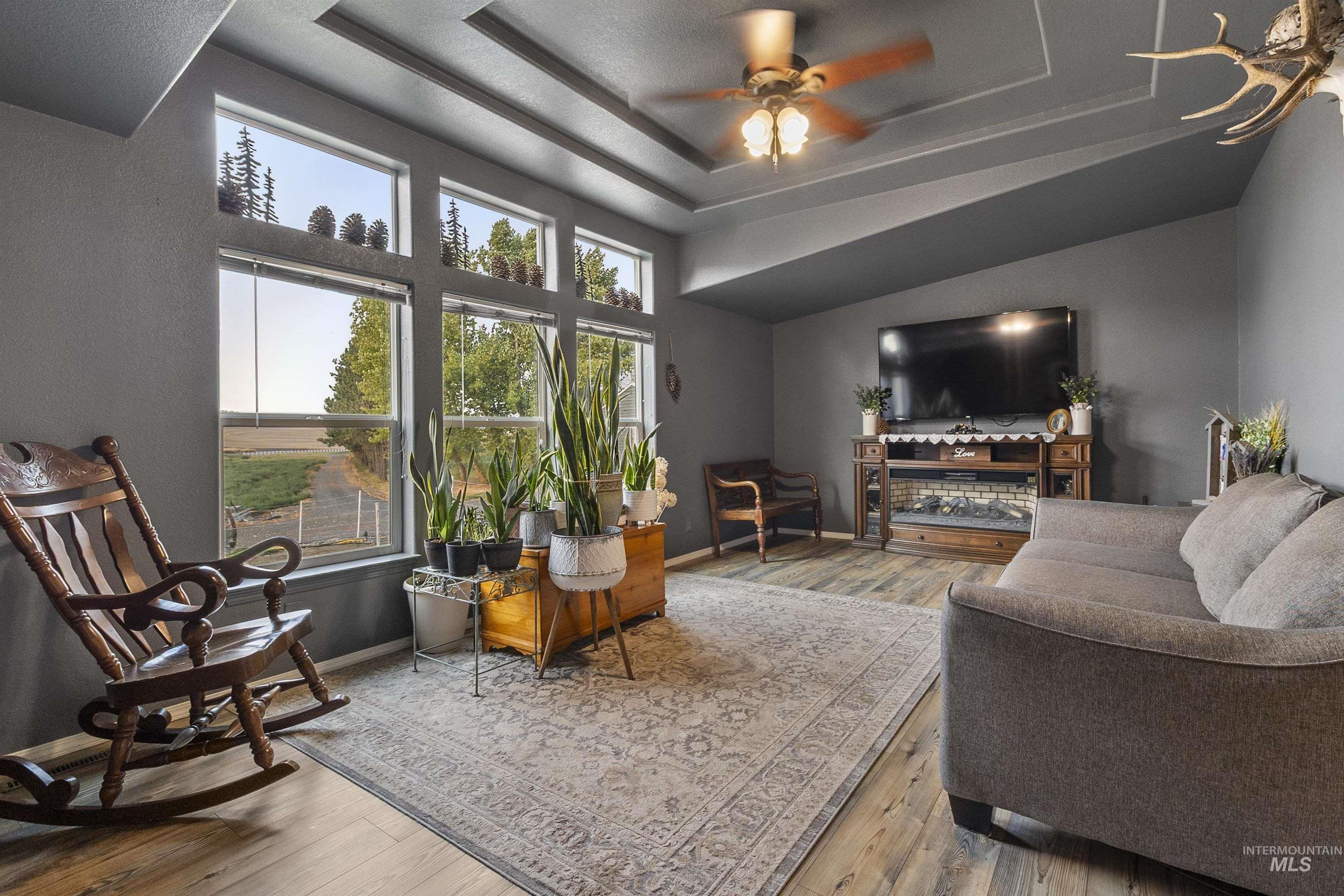Living room featuring a raised ceiling, wood finished floors, and a ceiling fan