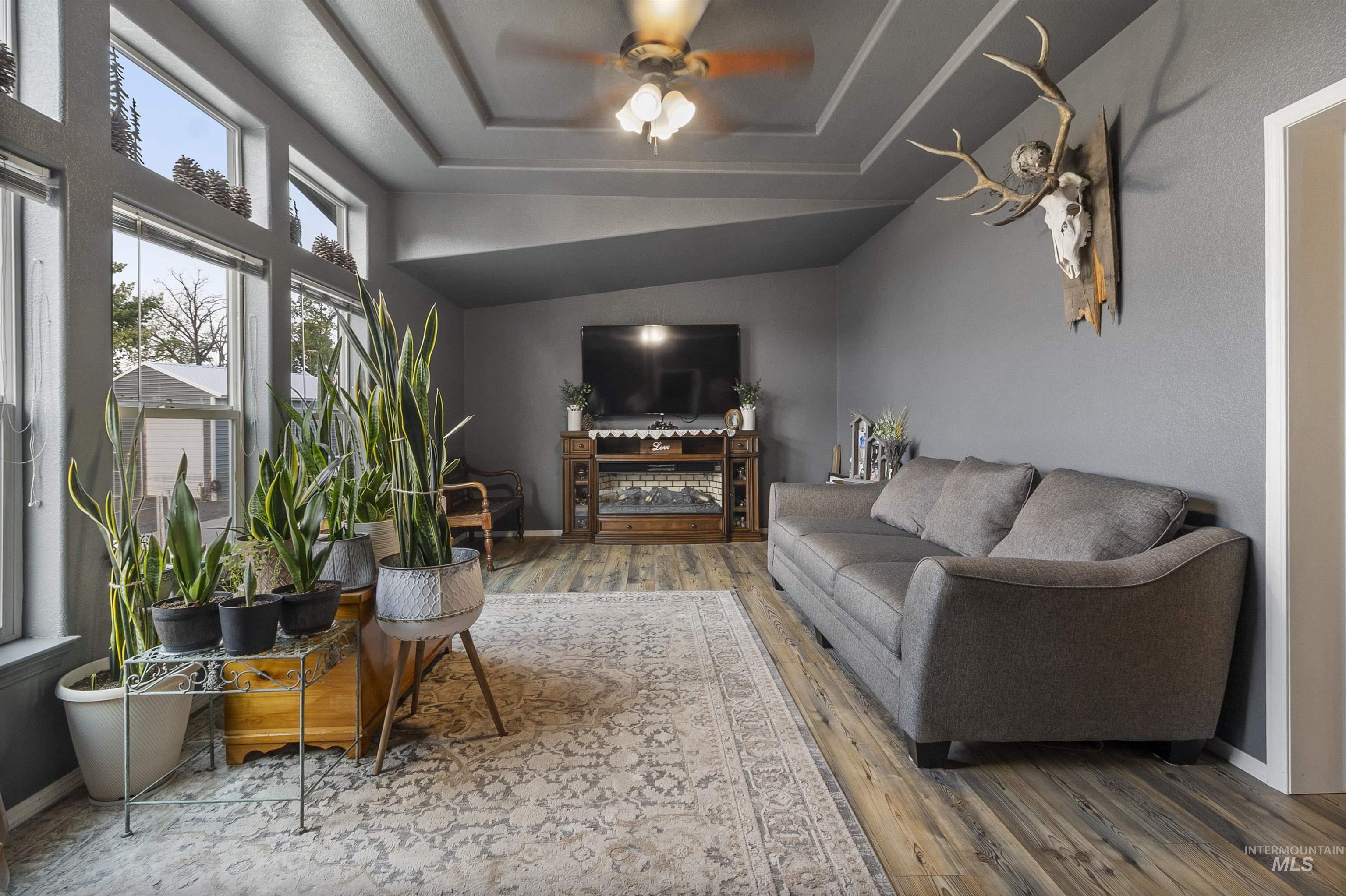 Living room featuring ceiling fan, a raised ceiling, and wood finished floors