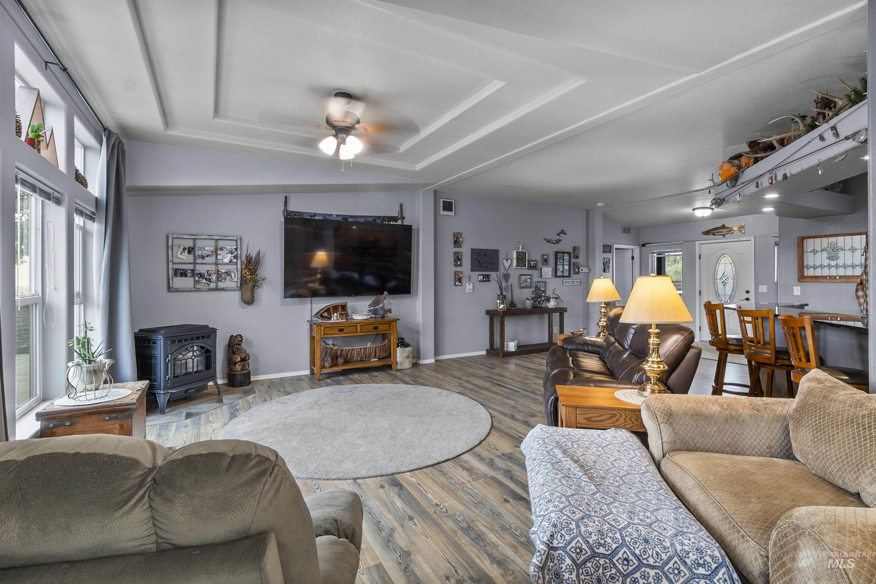 Living area featuring a wood stove, a raised ceiling, wood finished floors, and a ceiling fan