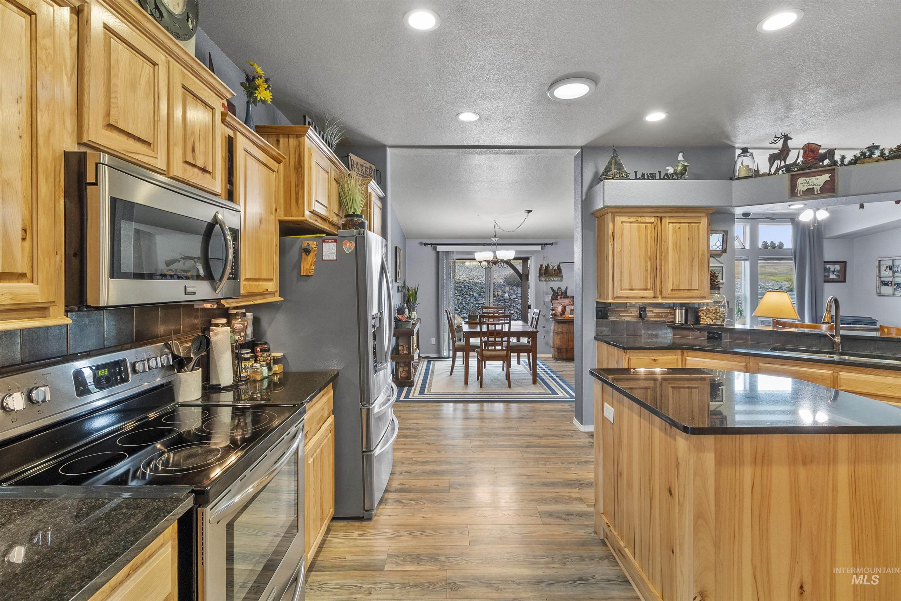 Kitchen with appliances with stainless steel finishes, a textured ceiling, dark stone countertops, light wood-style floors, and plenty of natural light