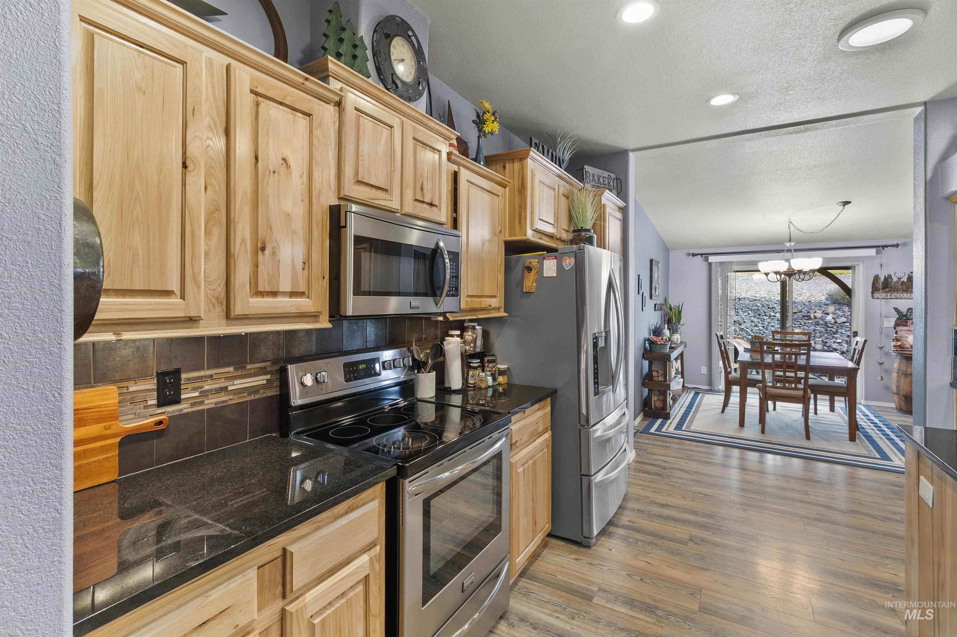 Kitchen with stainless steel appliances, backsplash, light wood-type flooring, a chandelier, and light brown cabinetry