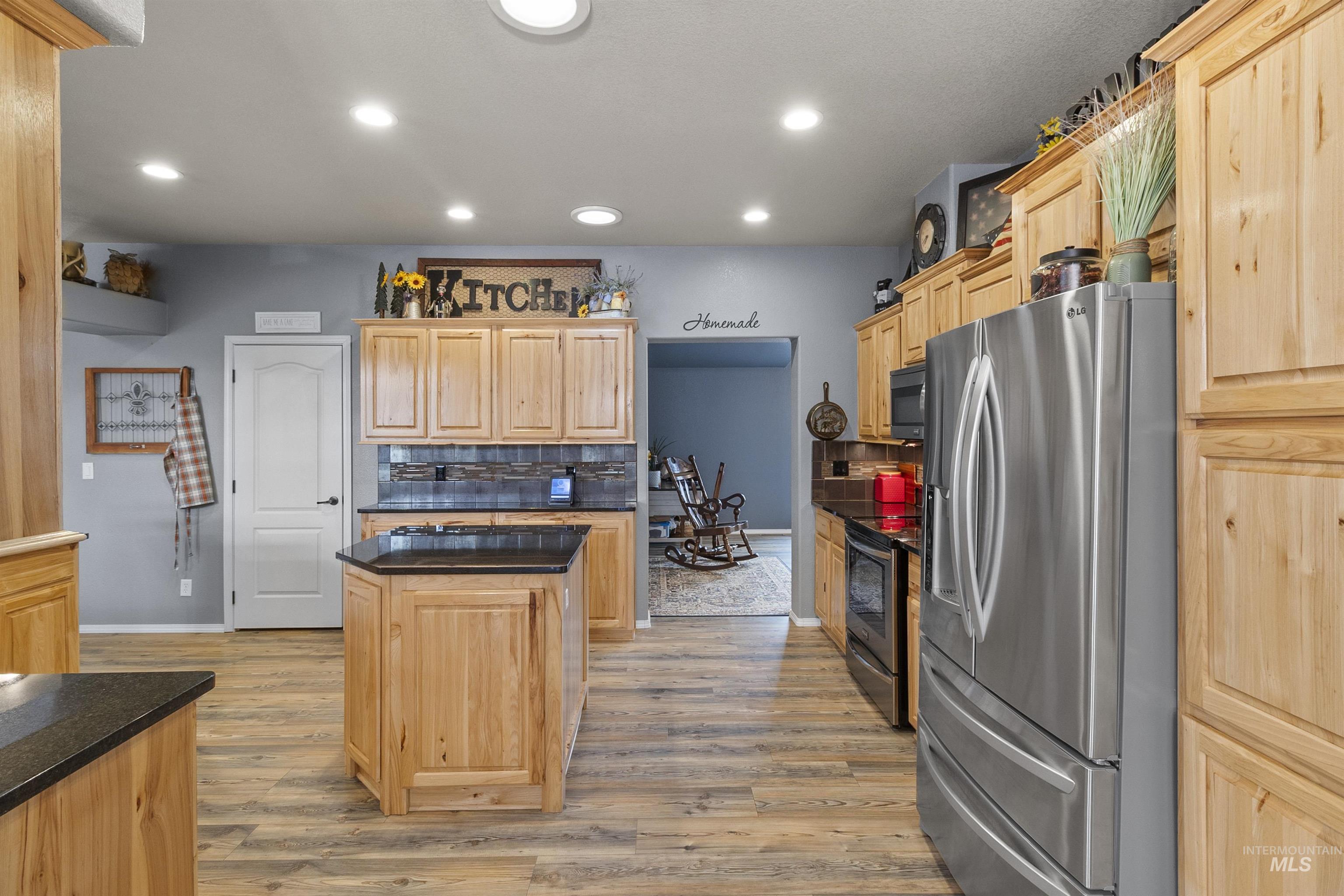 Kitchen with stainless steel appliances, light brown cabinets, recessed lighting, light wood finished floors, and decorative backsplash