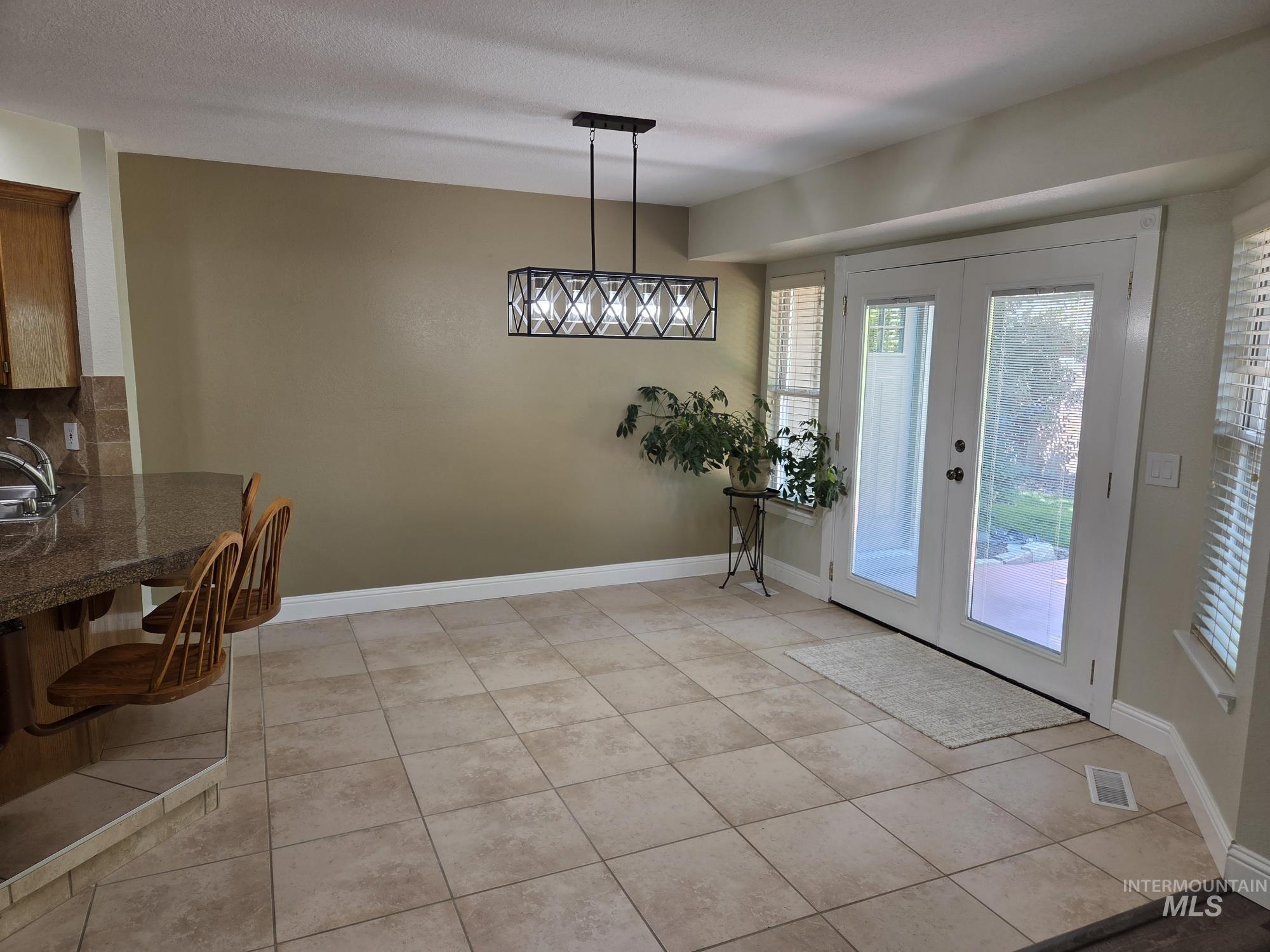 Dining space featuring french doors, light tile patterned flooring, and a textured ceiling