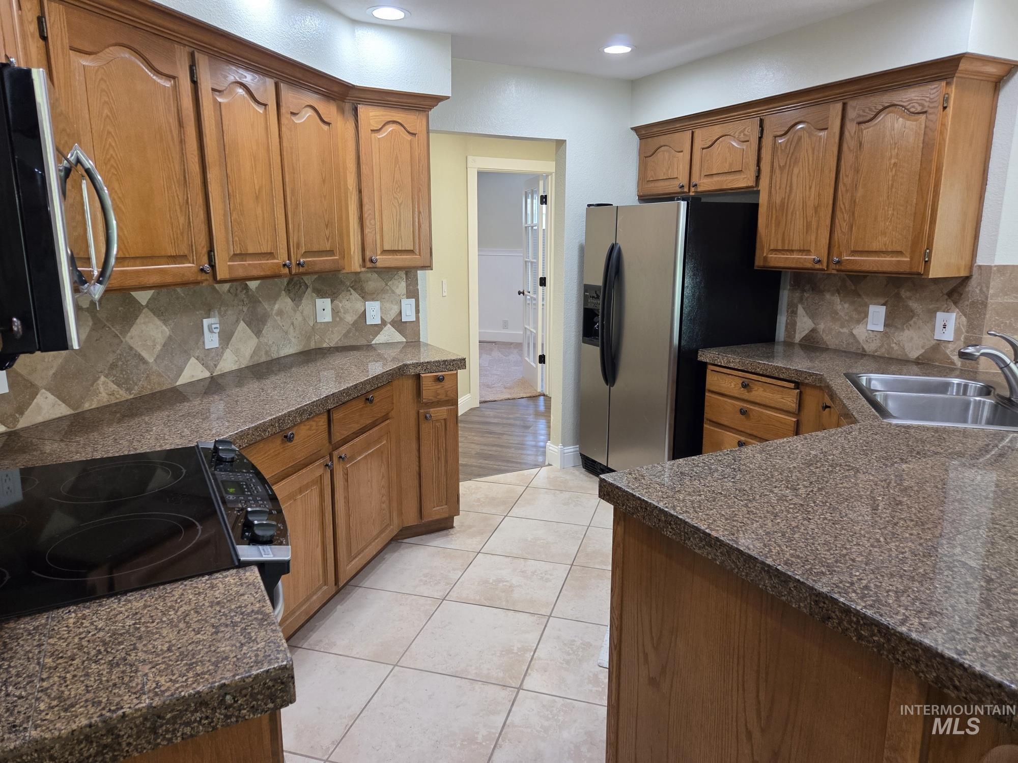 Kitchen with backsplash, brown cabinets, stainless steel appliances, light tile patterned flooring, and recessed lighting