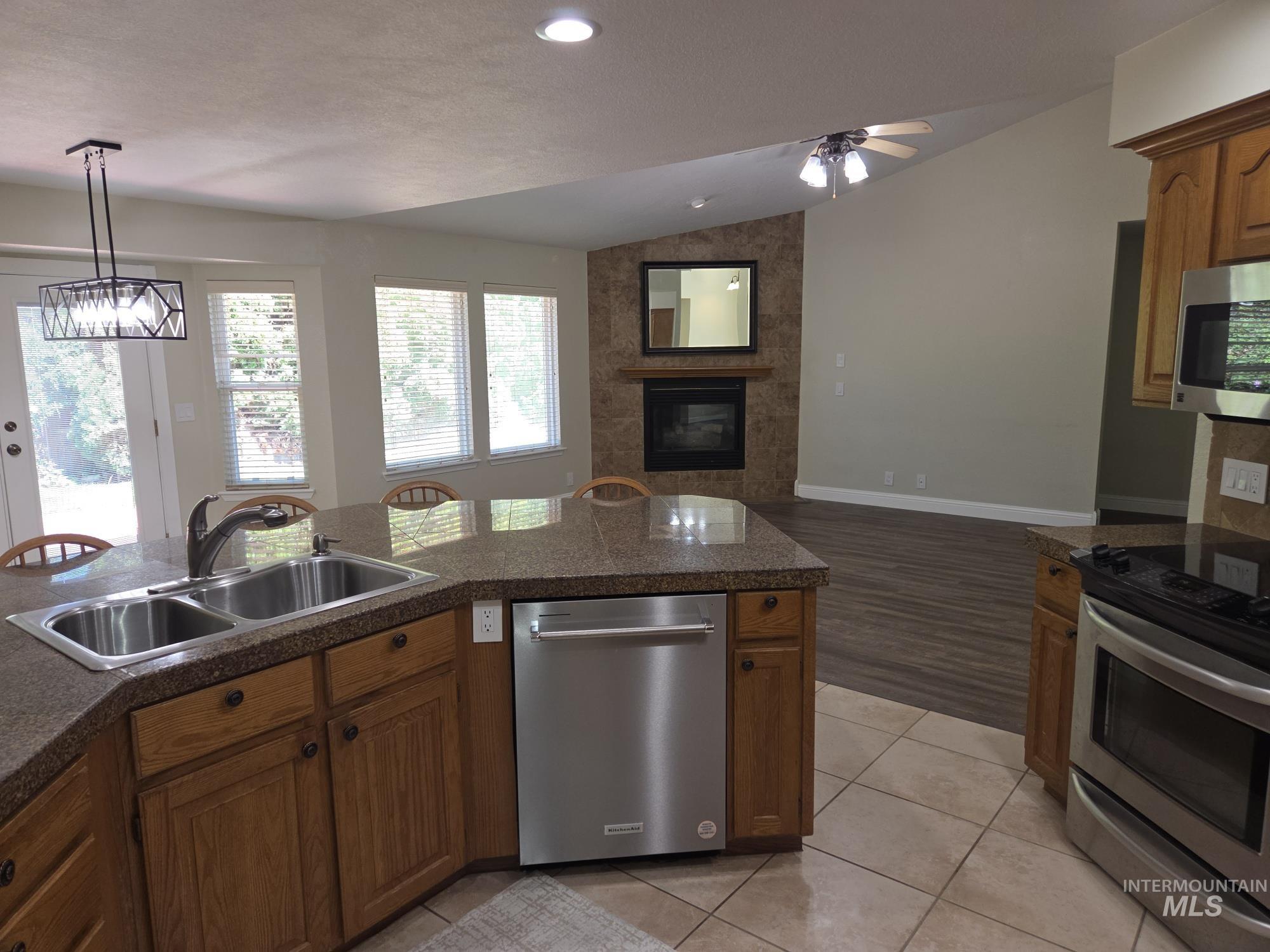 Kitchen with stainless steel appliances, vaulted ceiling, brown cabinetry, hanging light fixtures, and open floor plan