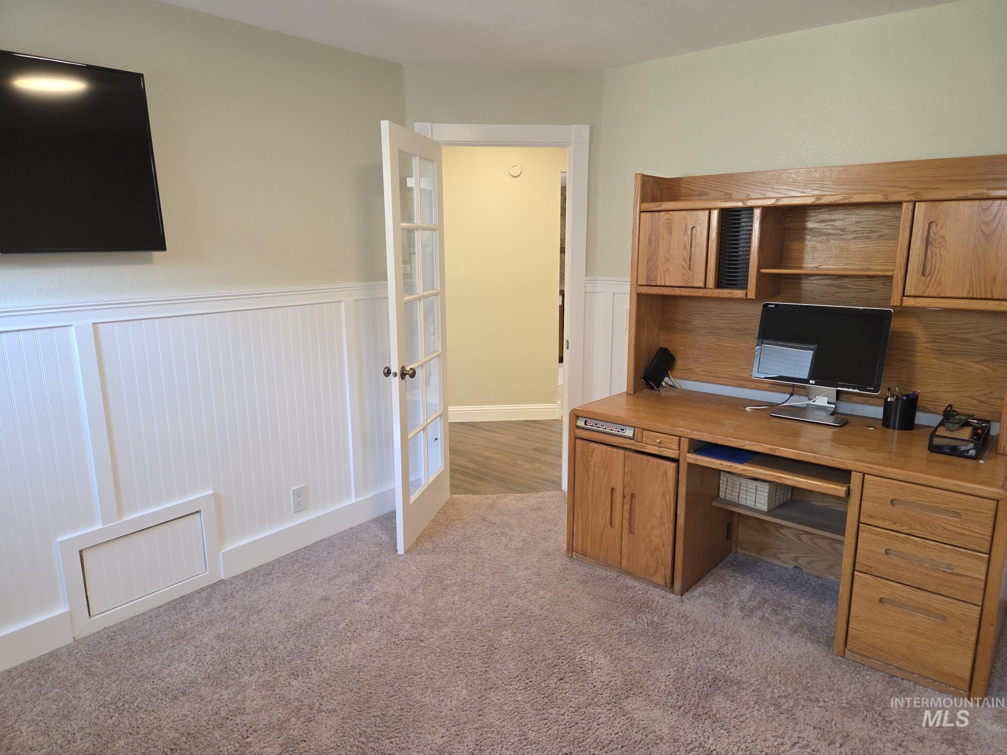 Office featuring wainscoting, light carpet, and a decorative wall
