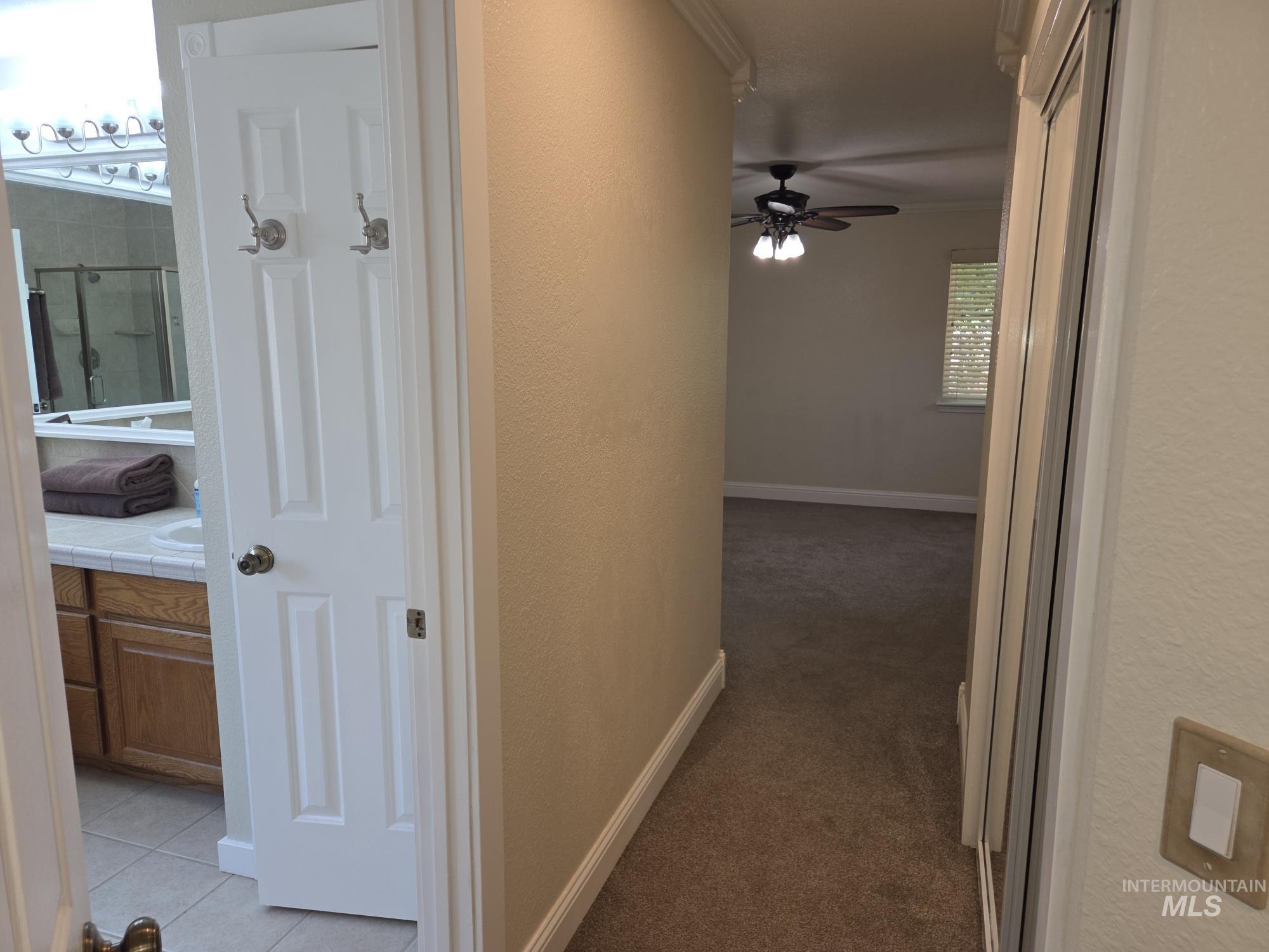 Corridor featuring a textured wall, light carpet, ornamental molding, and light tile patterned flooring