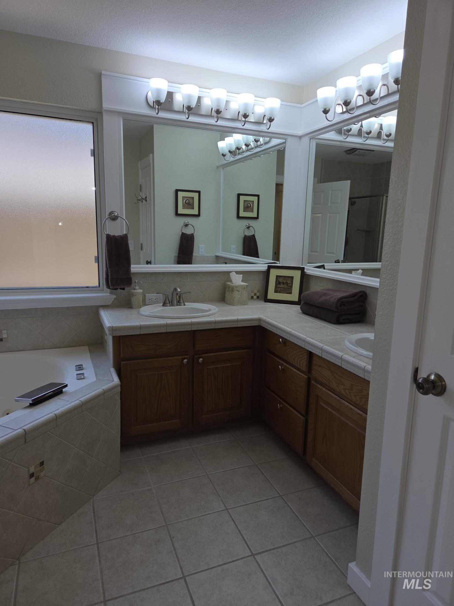 Bathroom featuring double vanity, light tile patterned flooring, a shower stall, and a garden tub